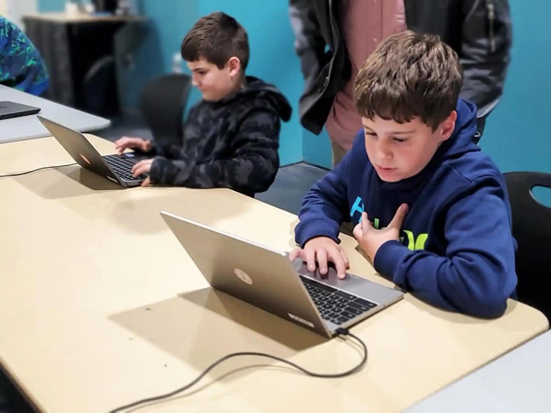 a group of boys sitting at a table with laptops