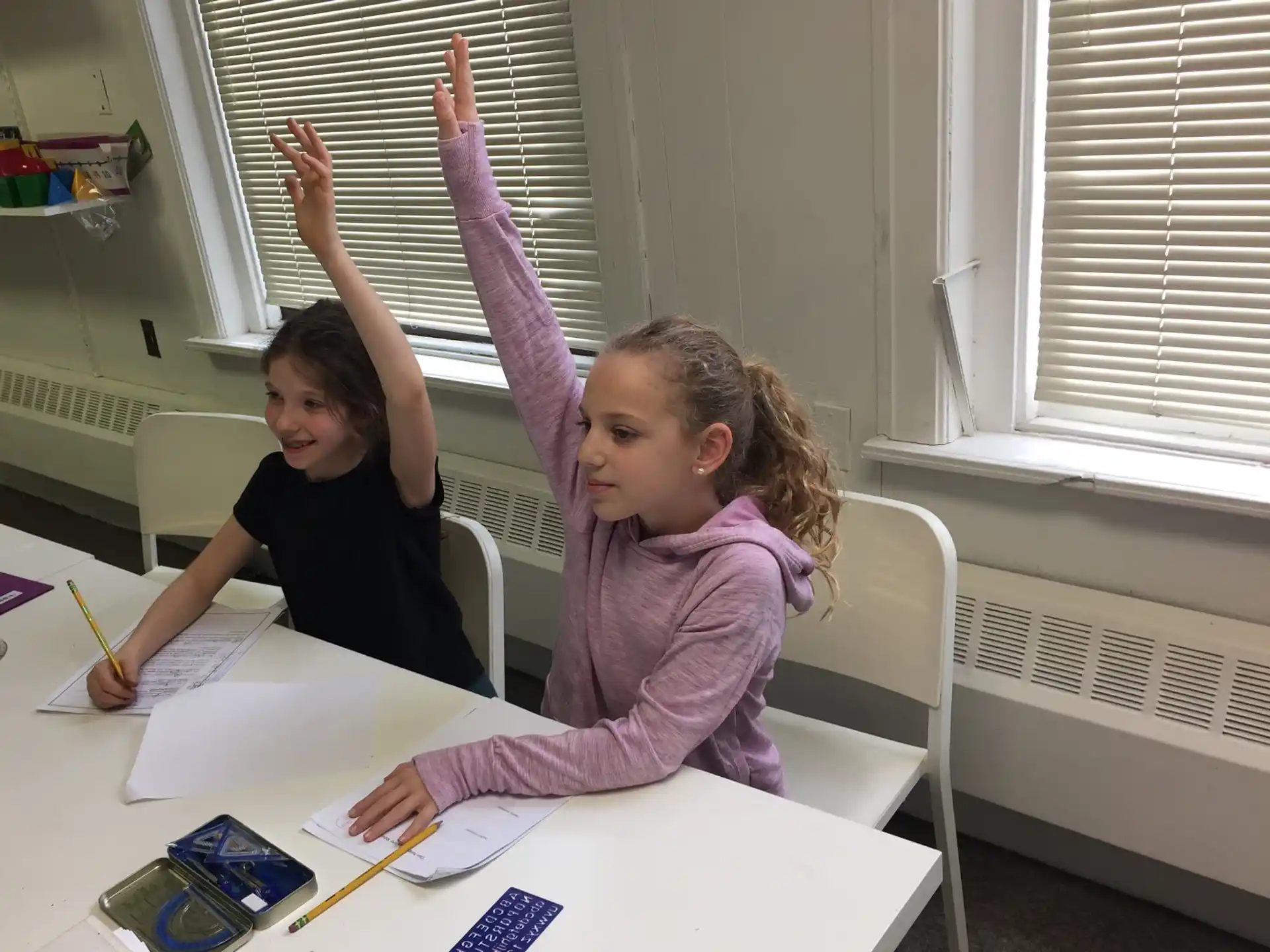 a couple of girls sitting at a table with a paper and pencils