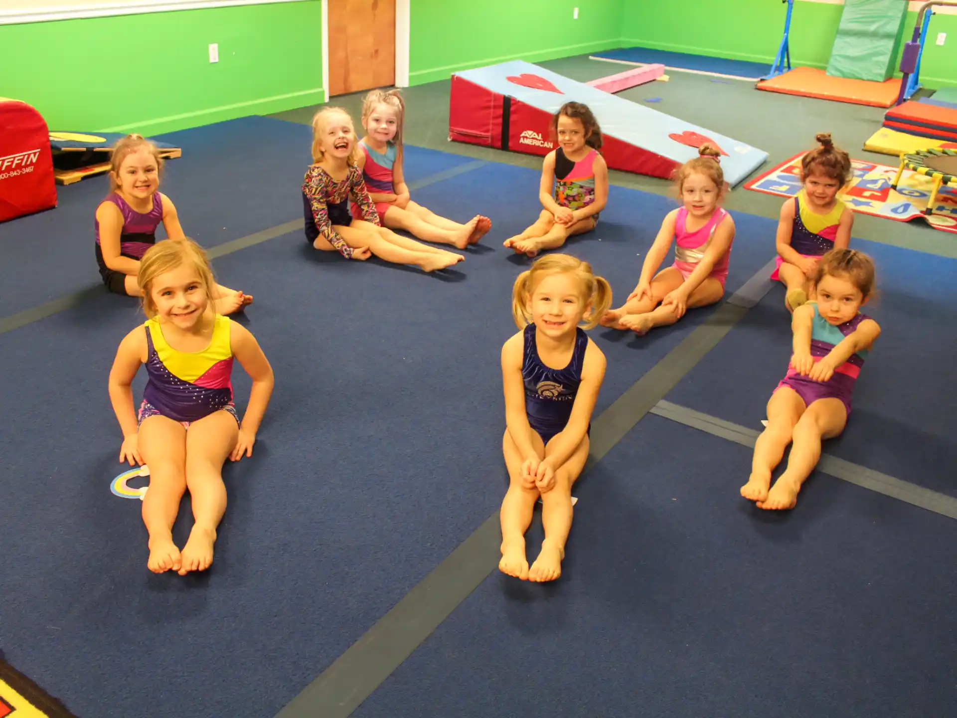 a group of children sitting on a mat in a gym