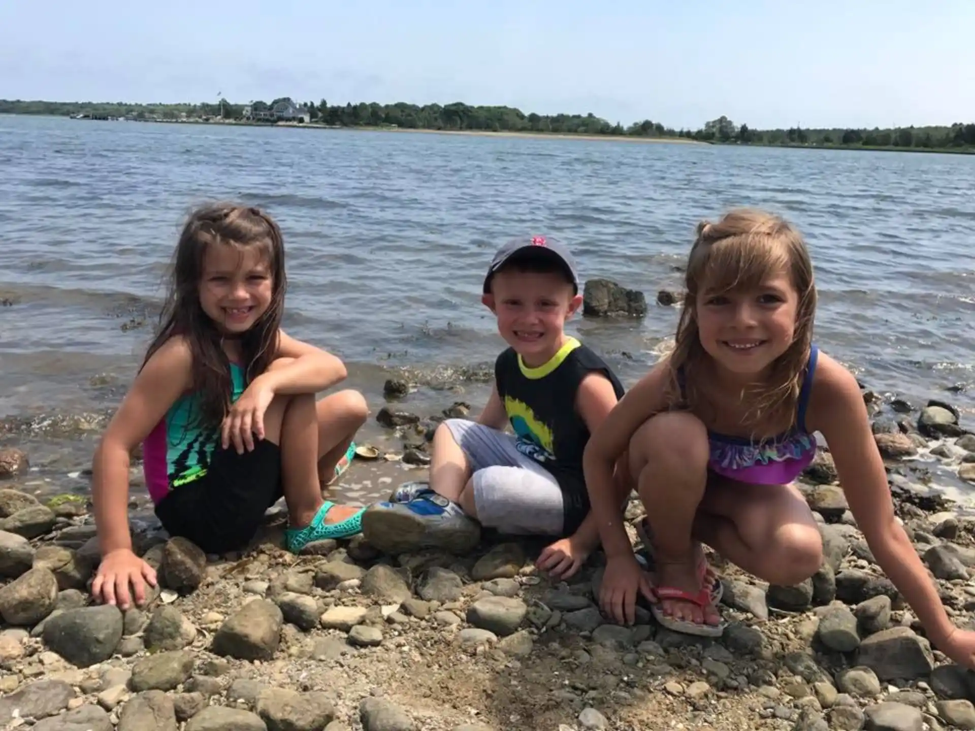 a group of girls sitting on rocks by a body of water