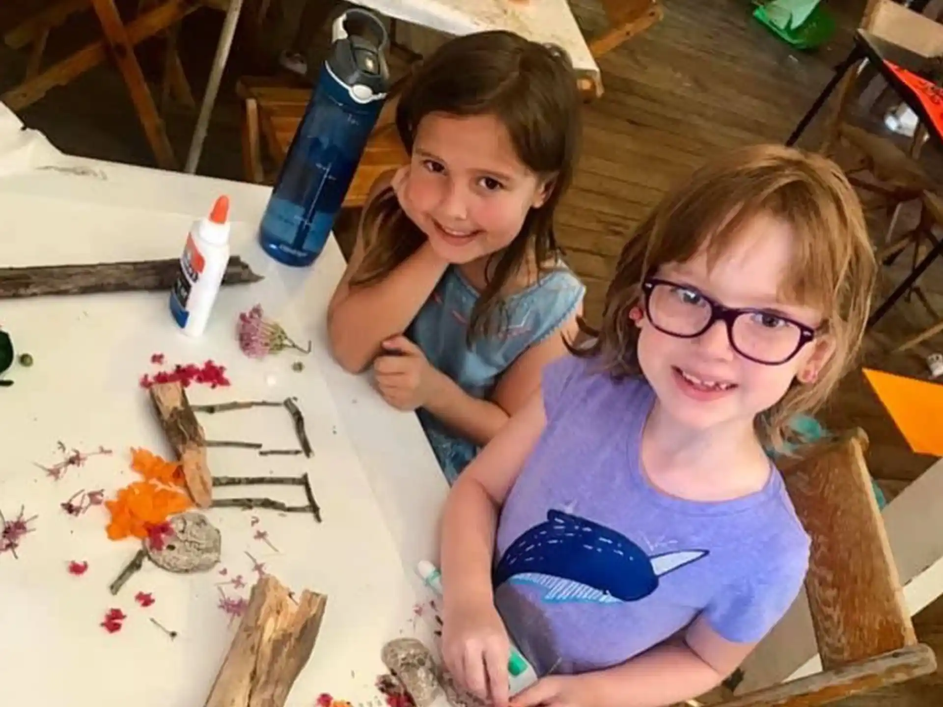 a couple of girls sitting at a table with art