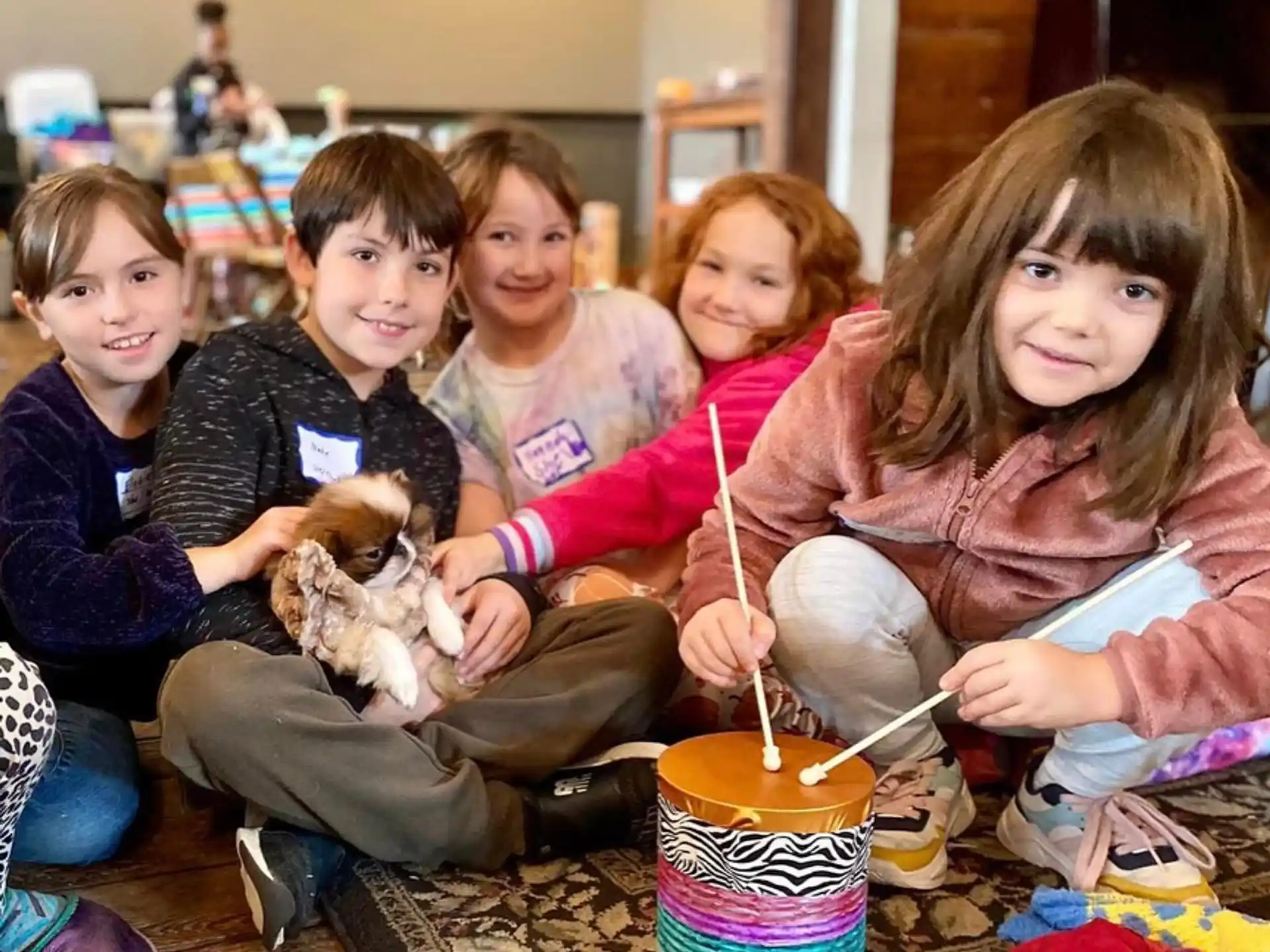 a group of children sitting on the floor with a dog and a cup