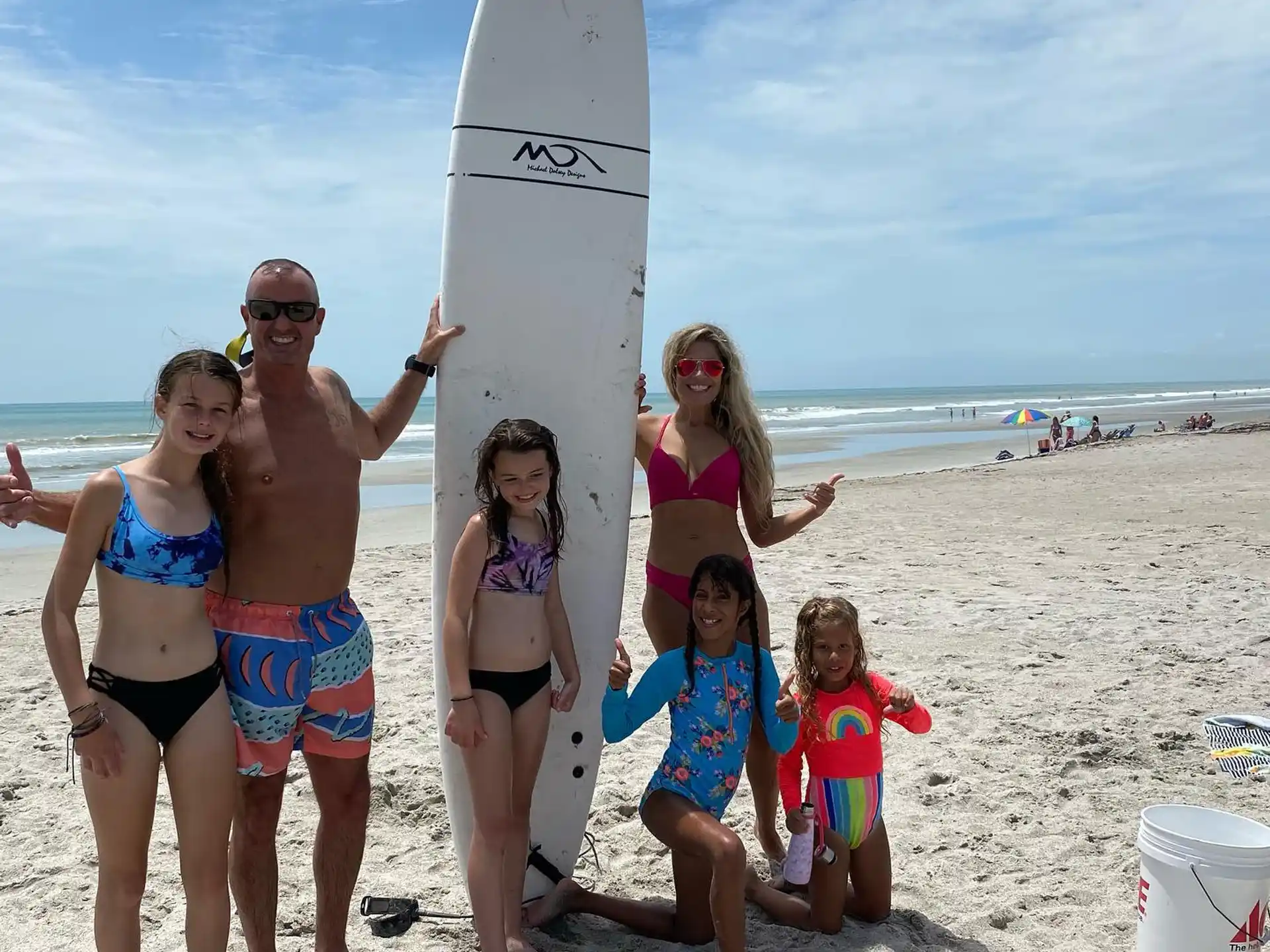 a group of women and children on a beach with a surfboard