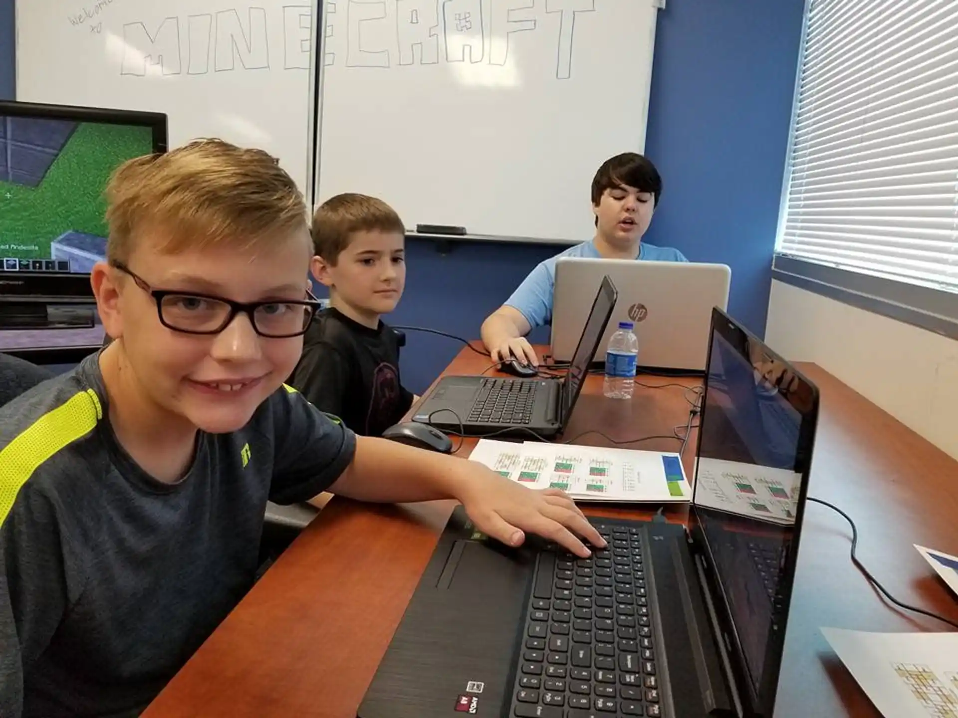 a group of boys sitting at a table with laptops