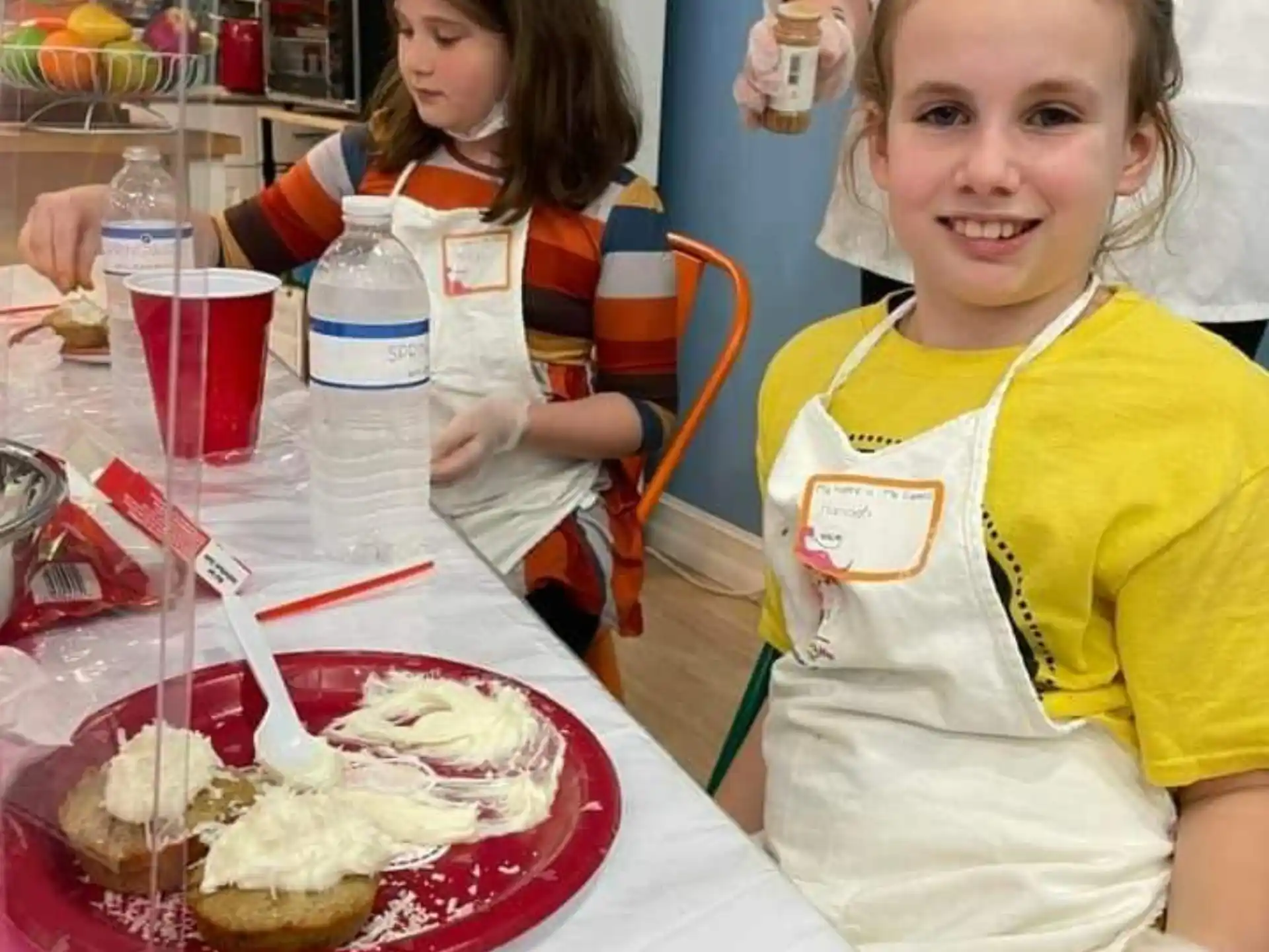 a couple of girls in aprons at a table with food