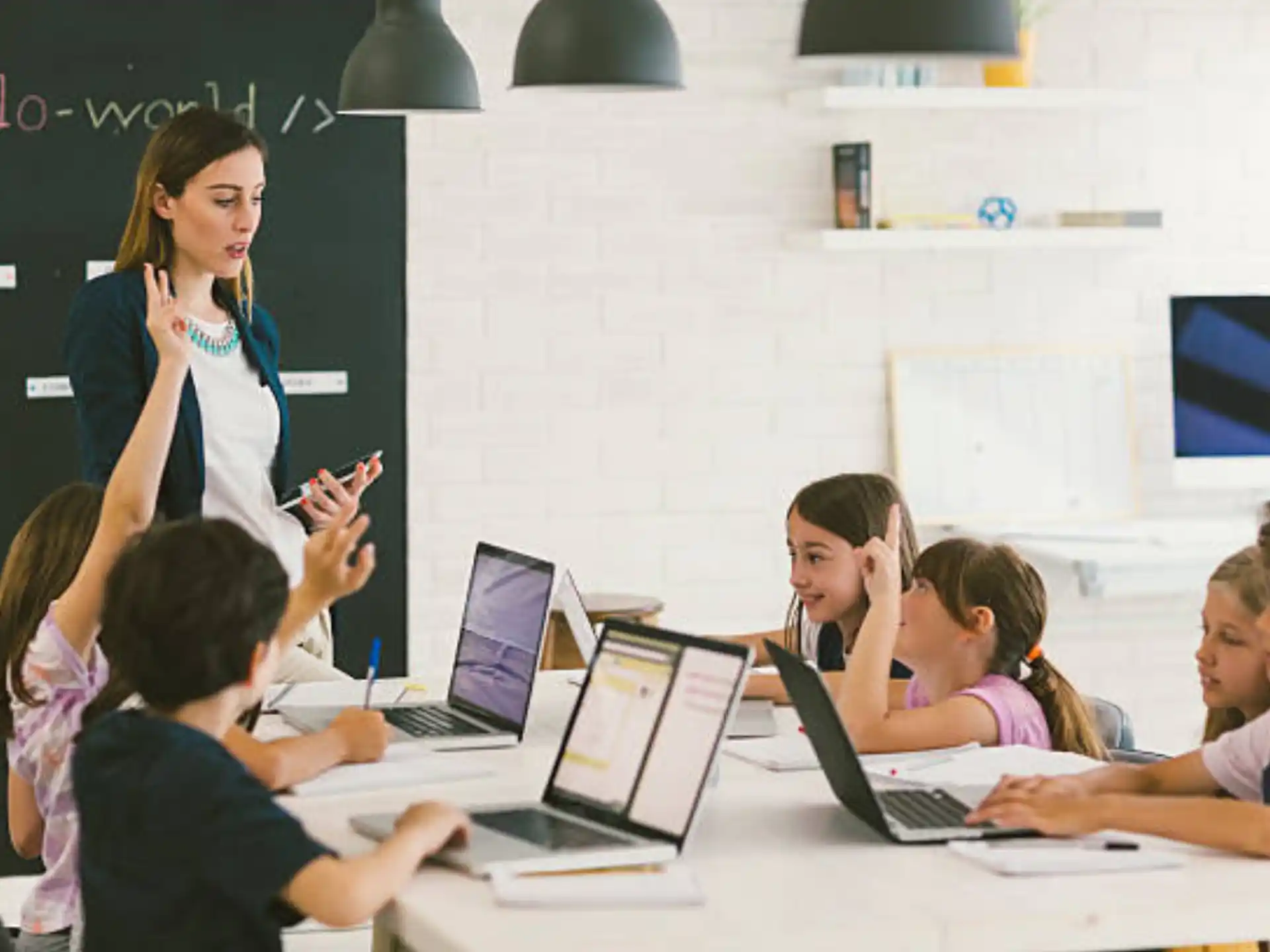 a person standing in front of a group of children using laptops