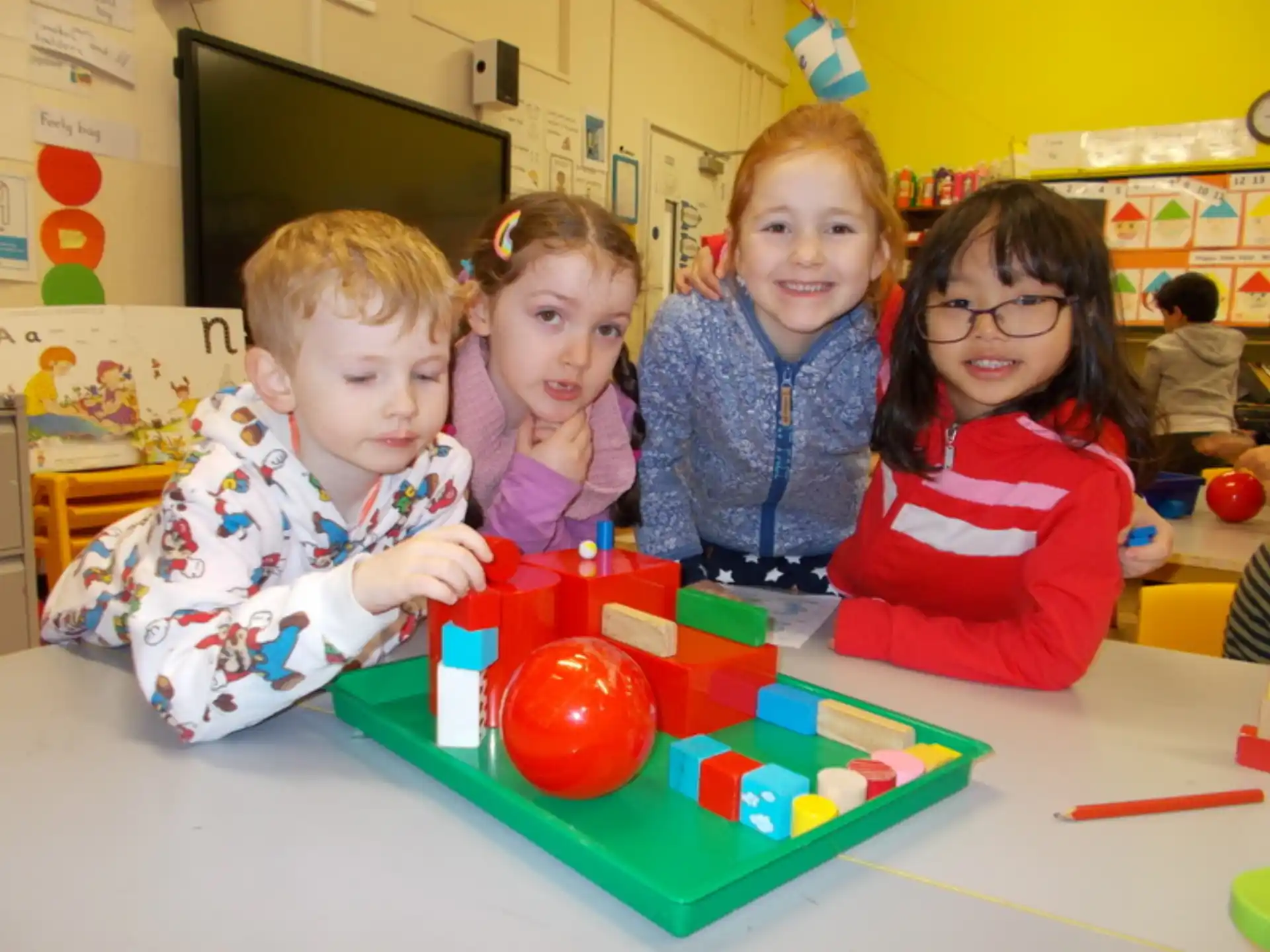 a group of children sitting at a table with a ball and a toy