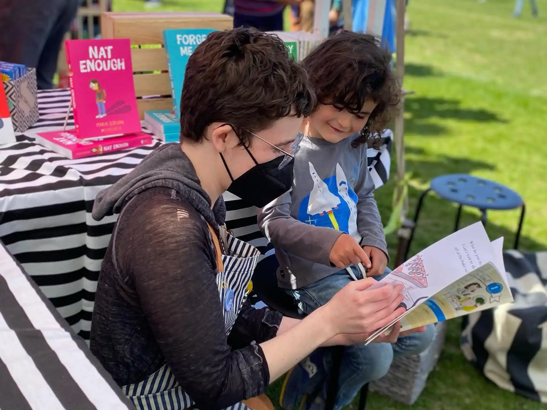 a person and a child sitting on a bench reading a book
