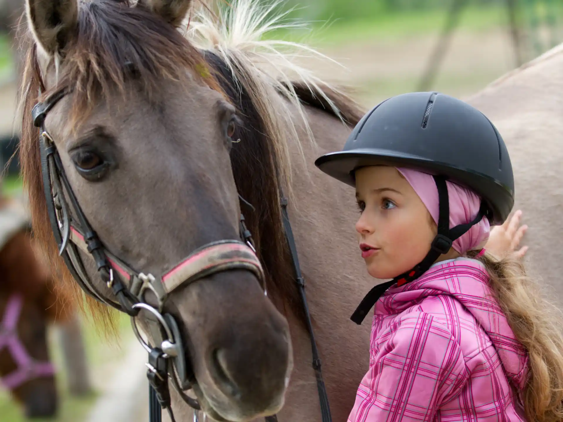 a girl with a helmet standing next to a horse