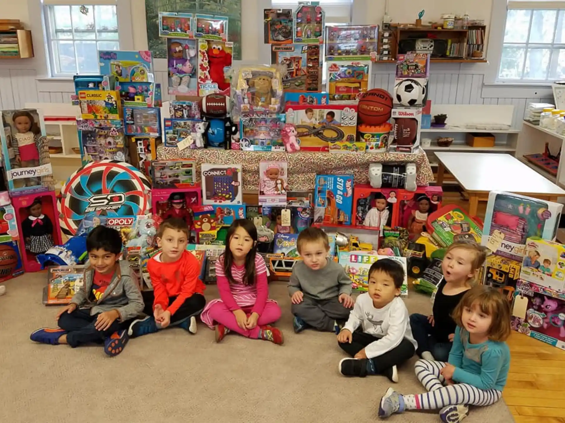 a group of children sitting on the floor in a room with a large bookcase and a table