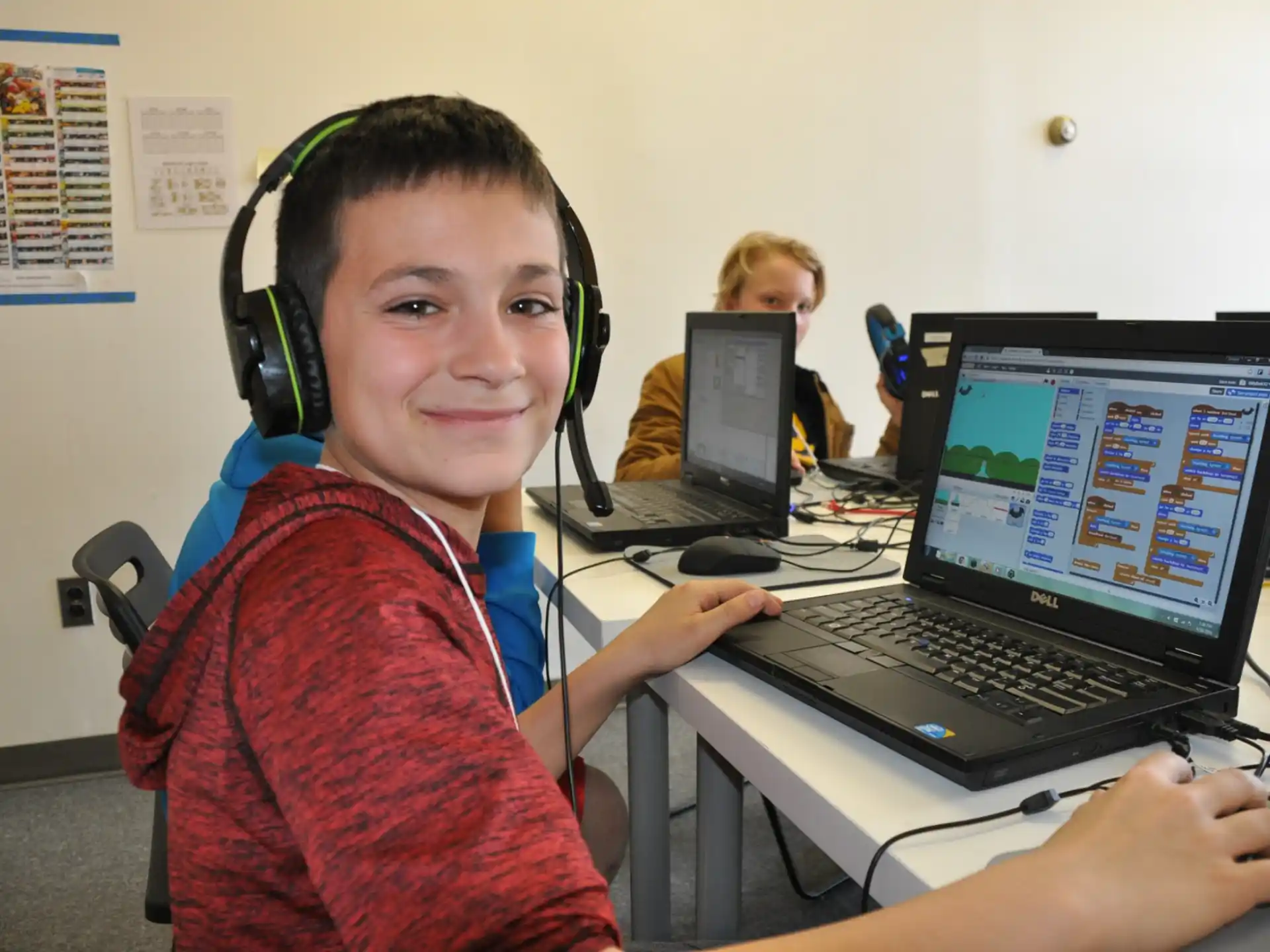 a boy wearing headphones and sitting at a desk with a laptop