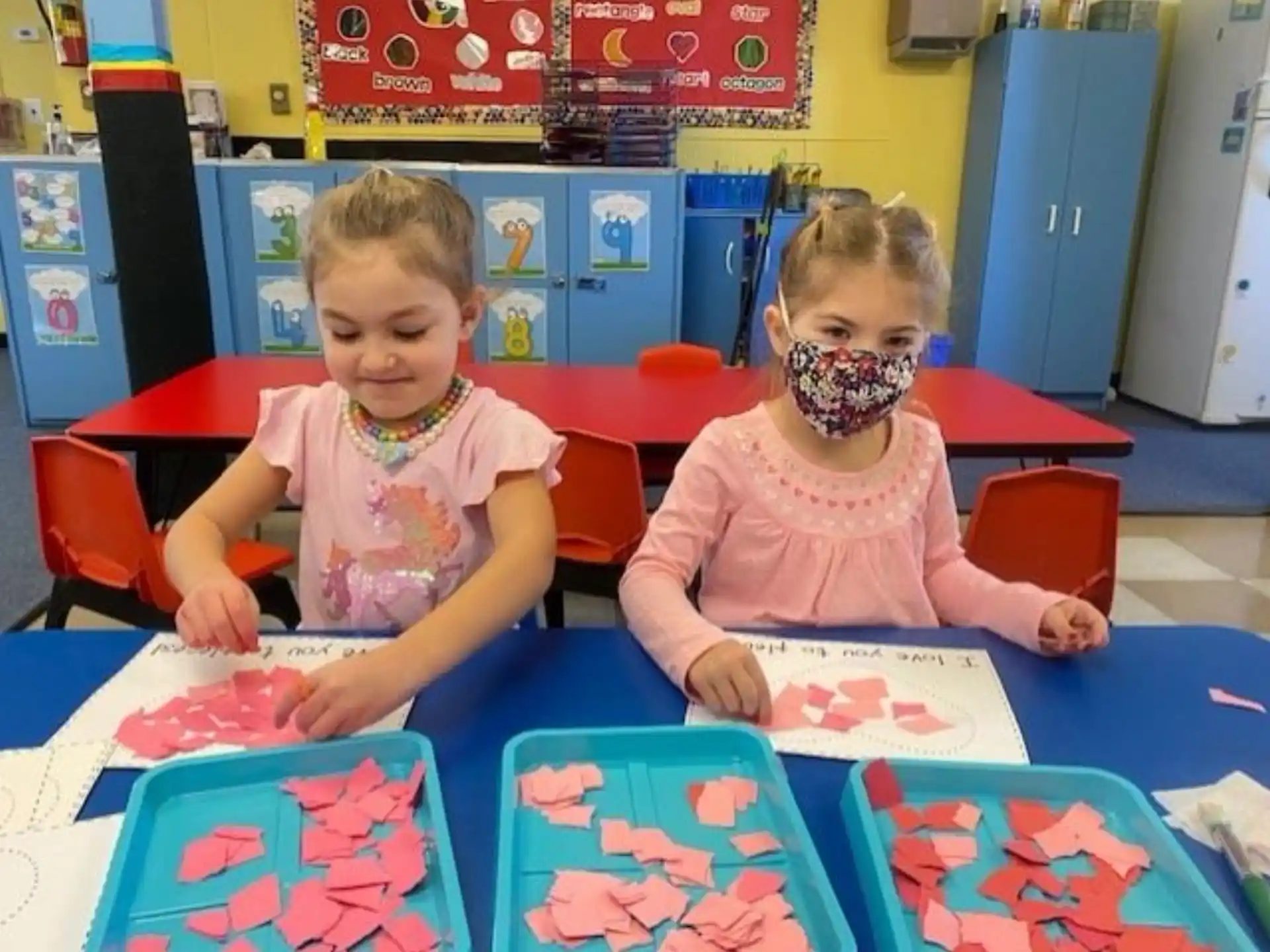 a couple of children sitting at a table with colorful paper on it