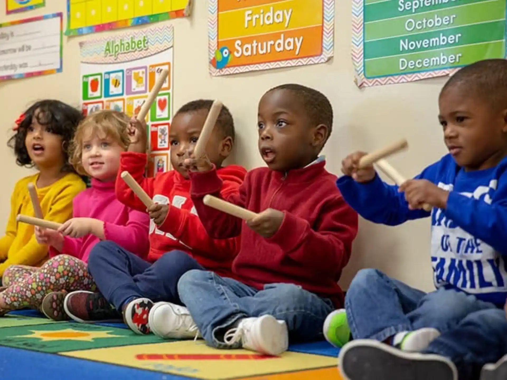 a group of children sitting on the floor holding wooden sticks