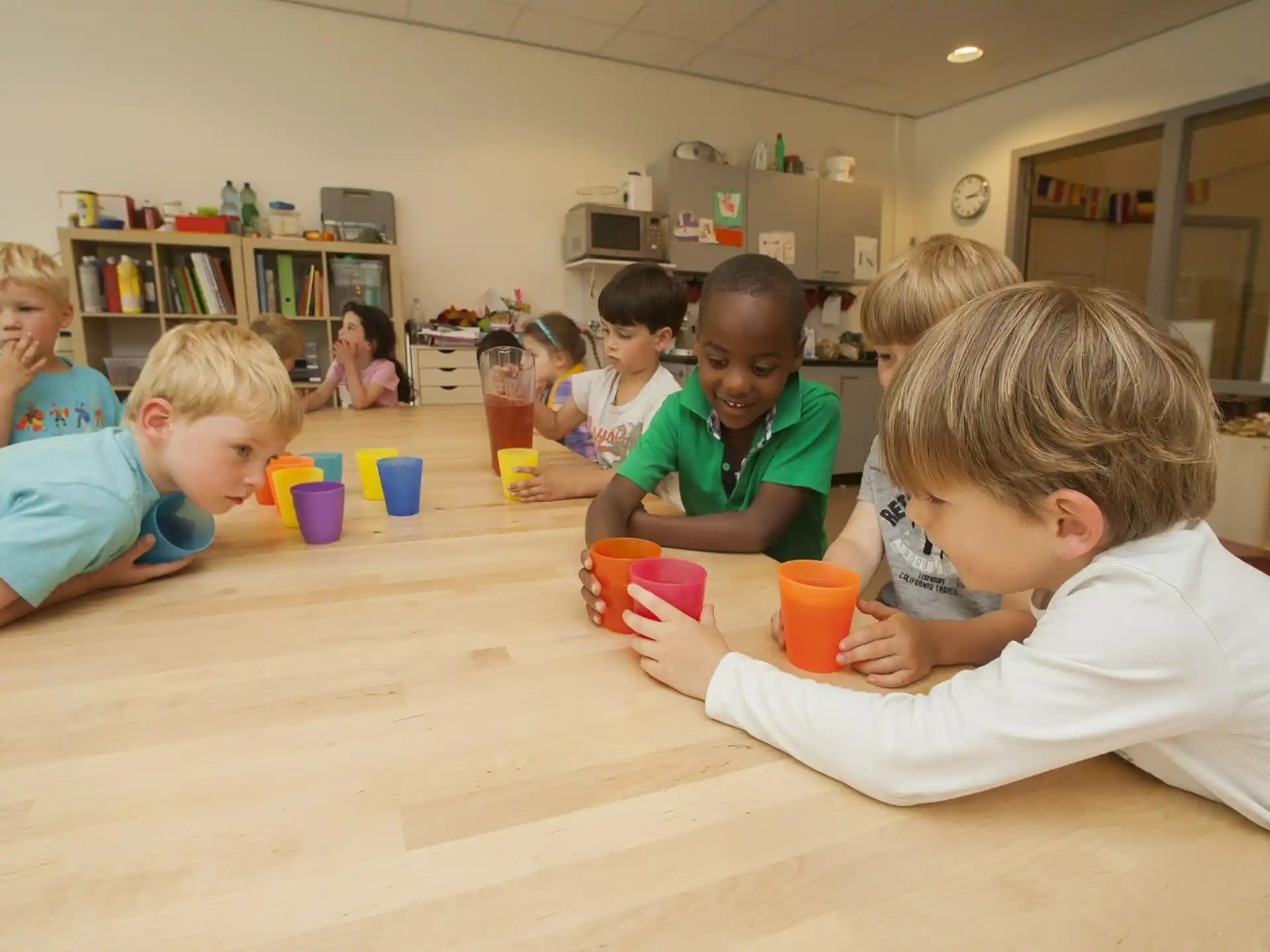 a group of children sitting at a table with cups and a book