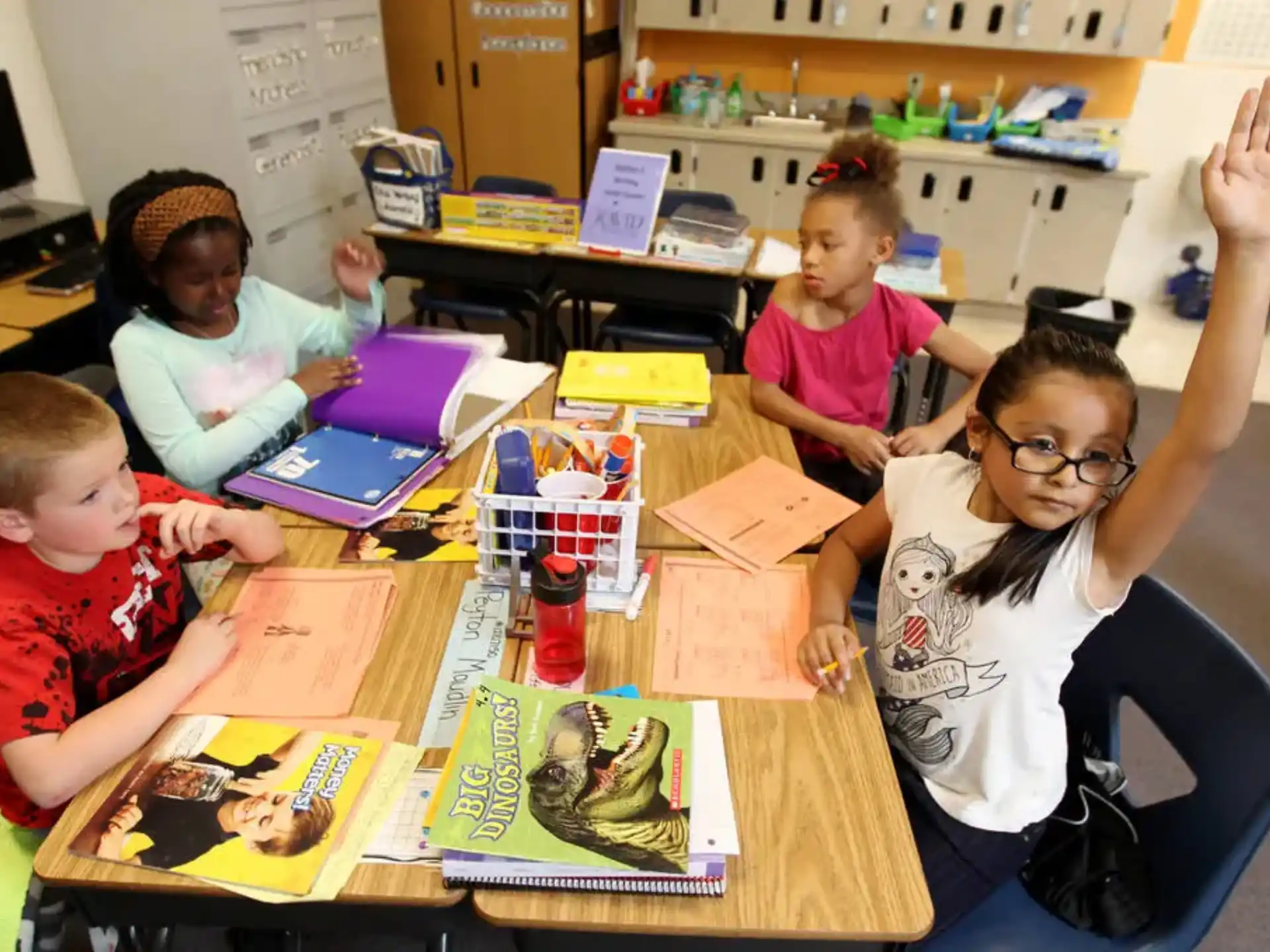 a group of children sitting at a table with books and a laptop