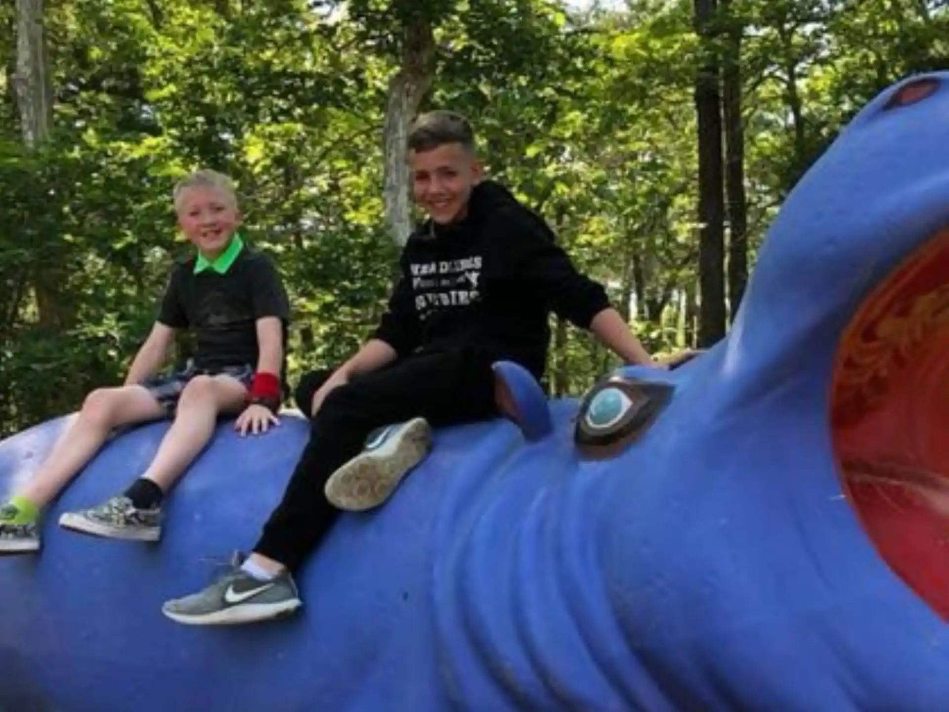 a group of boys sitting on a large blue and white slide in a forest