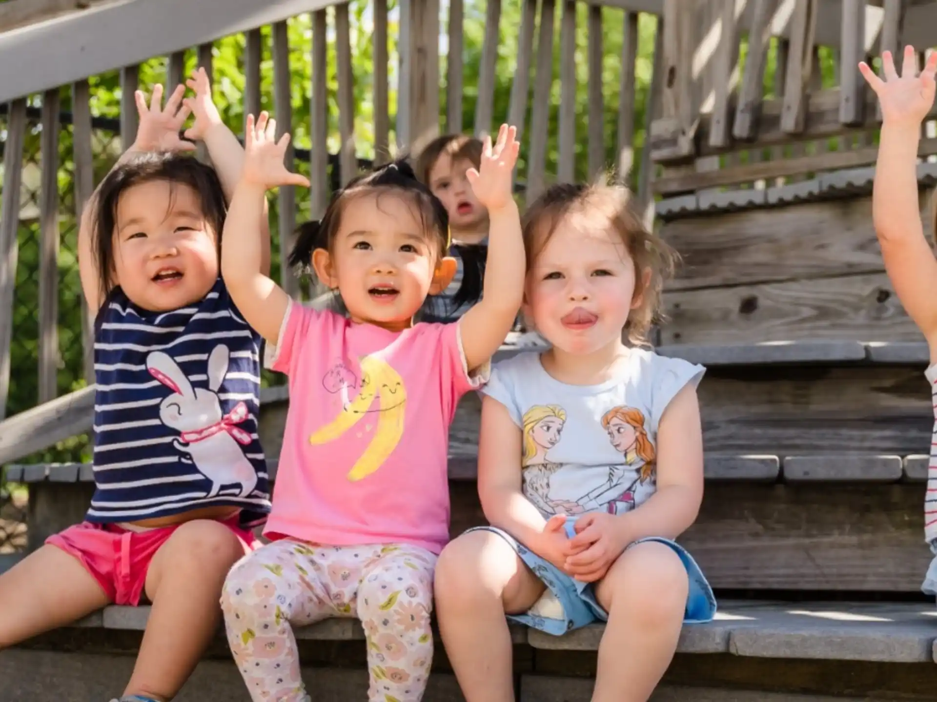 a group of children sitting on a bench with their arms raised