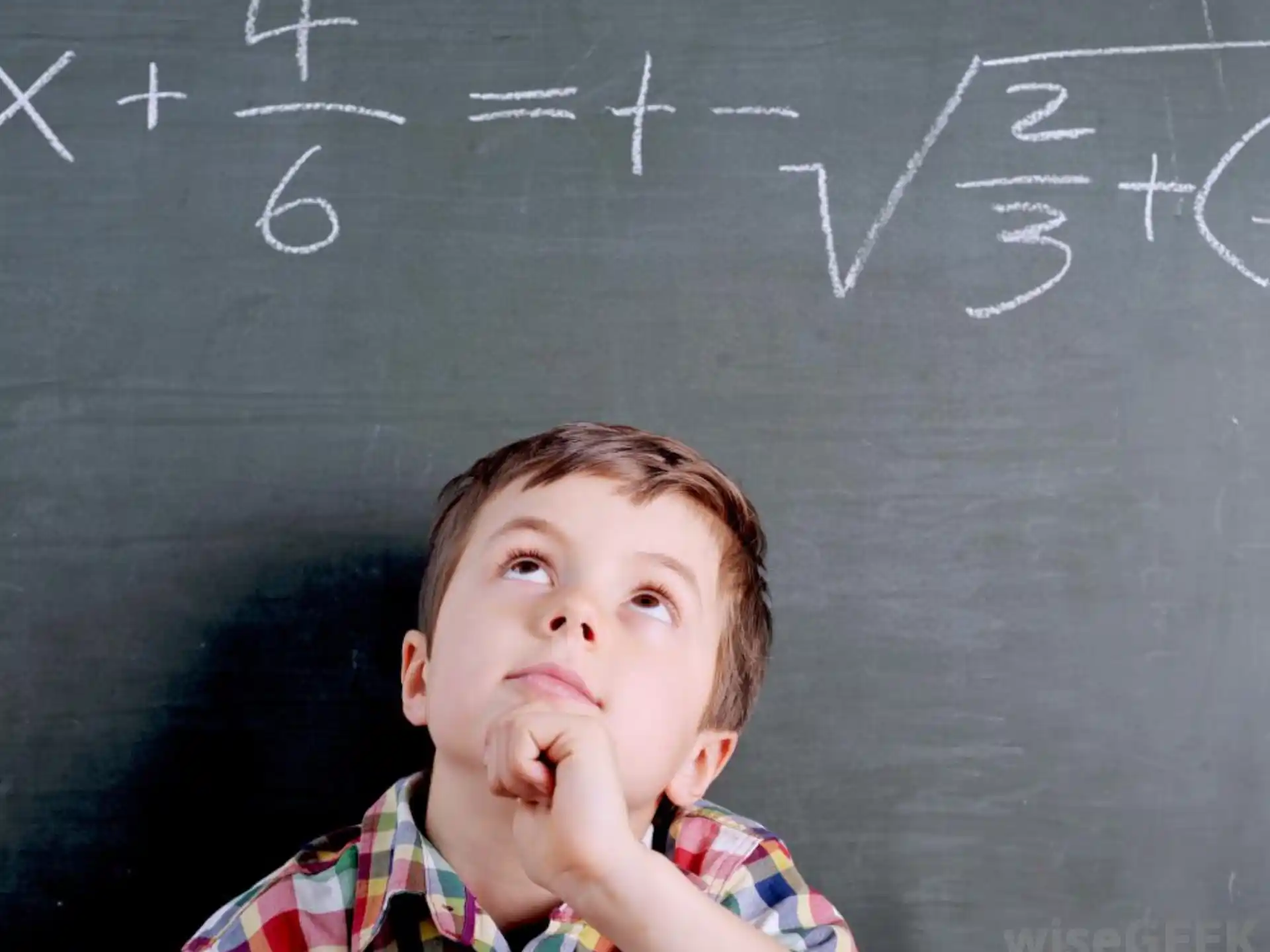 a boy with his hand on his chin in front of a chalkboard