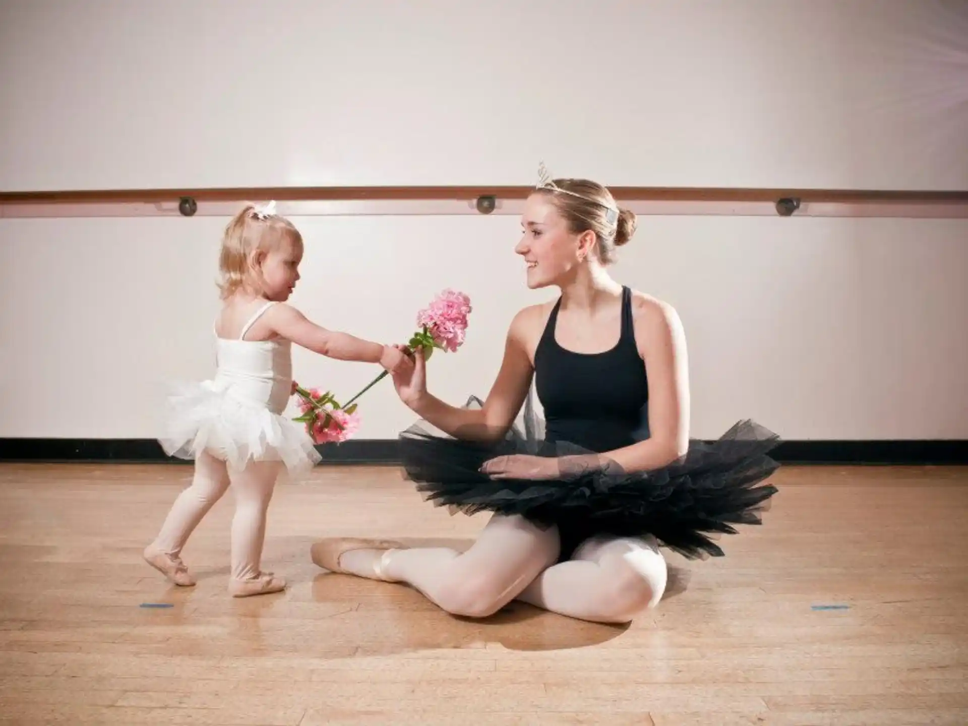 a woman kneeling next to a girl holding flowers