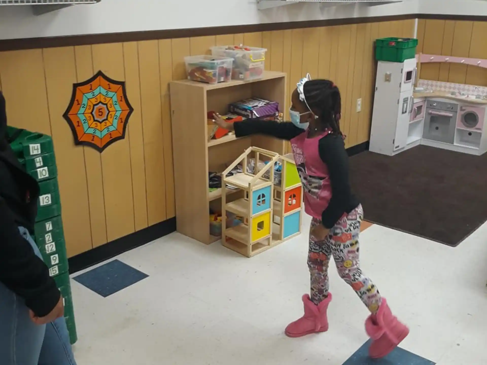 a girl in a room with a shelf and a table with objects on it