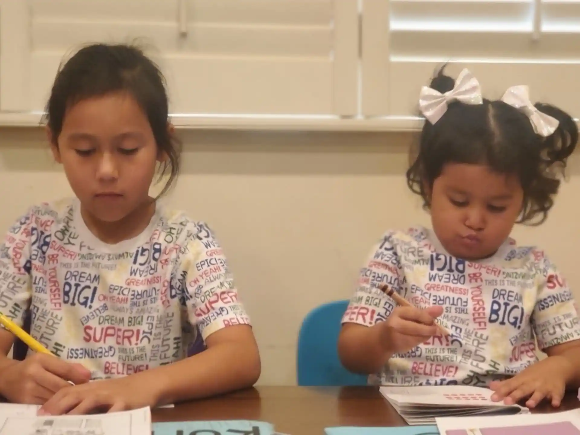 a couple of young girls sitting at a table writing on paper