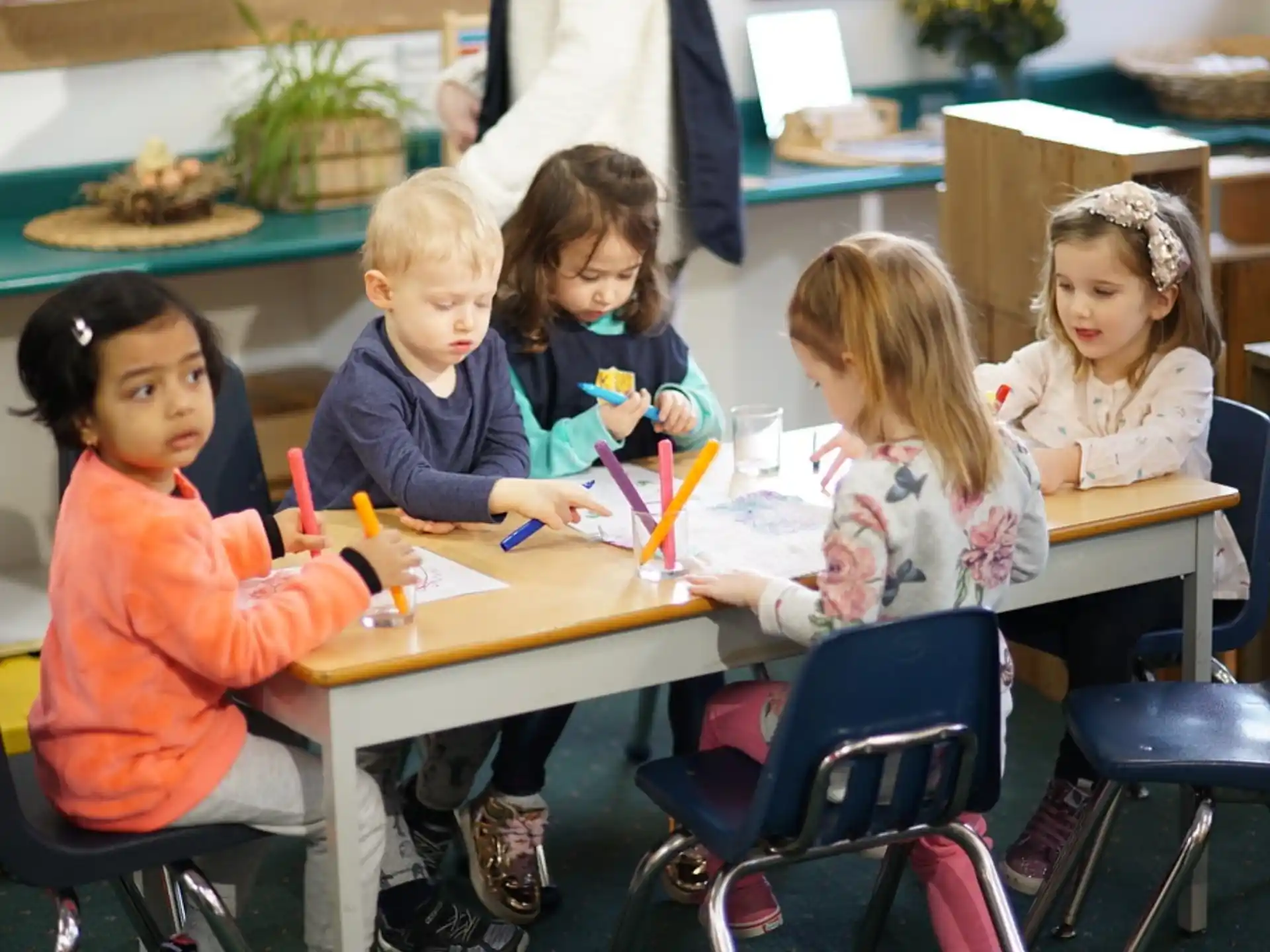 a group of children sitting at a table with colorful markers