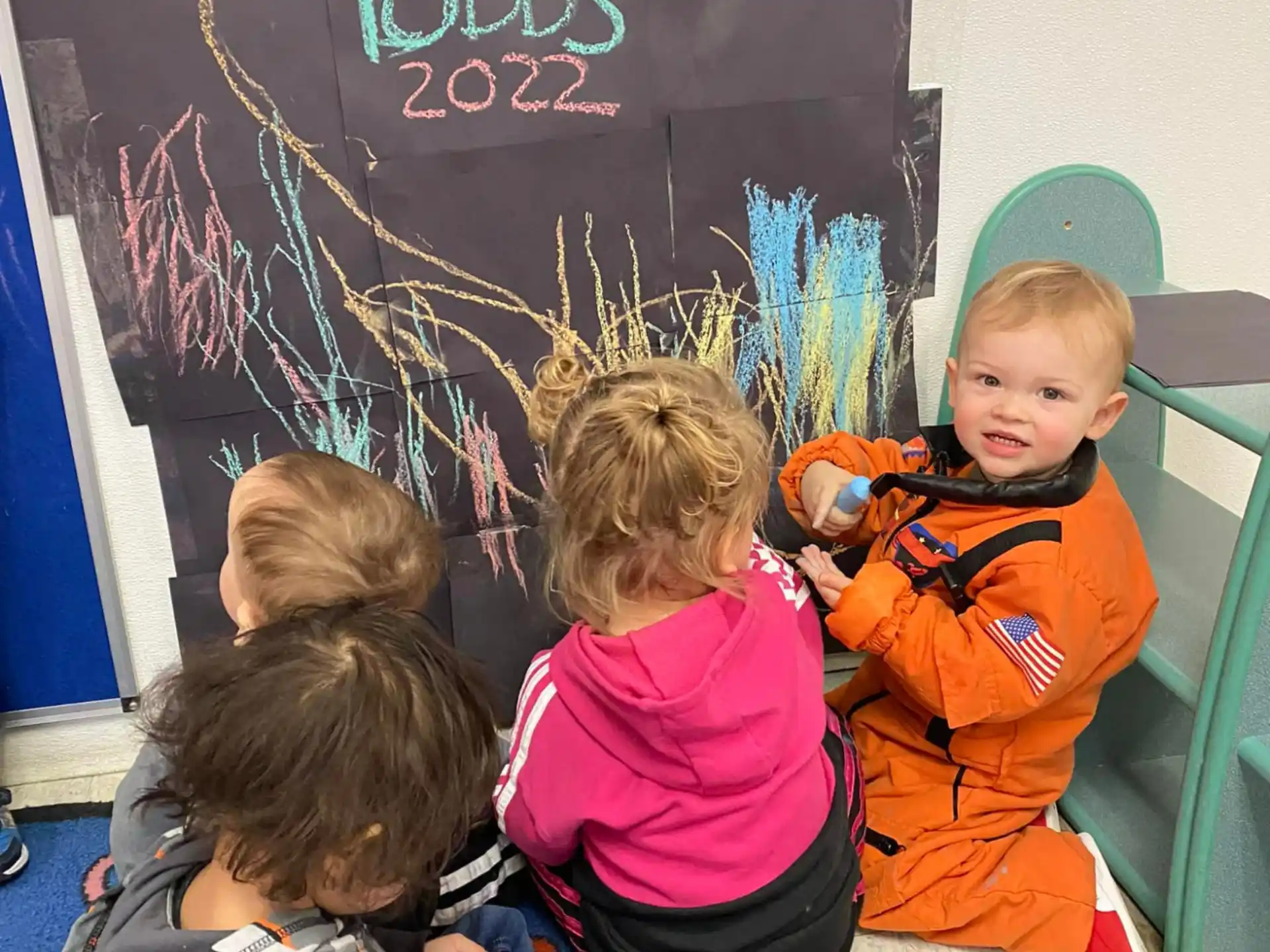 a group of children sitting on a bench in front of a chalkboard