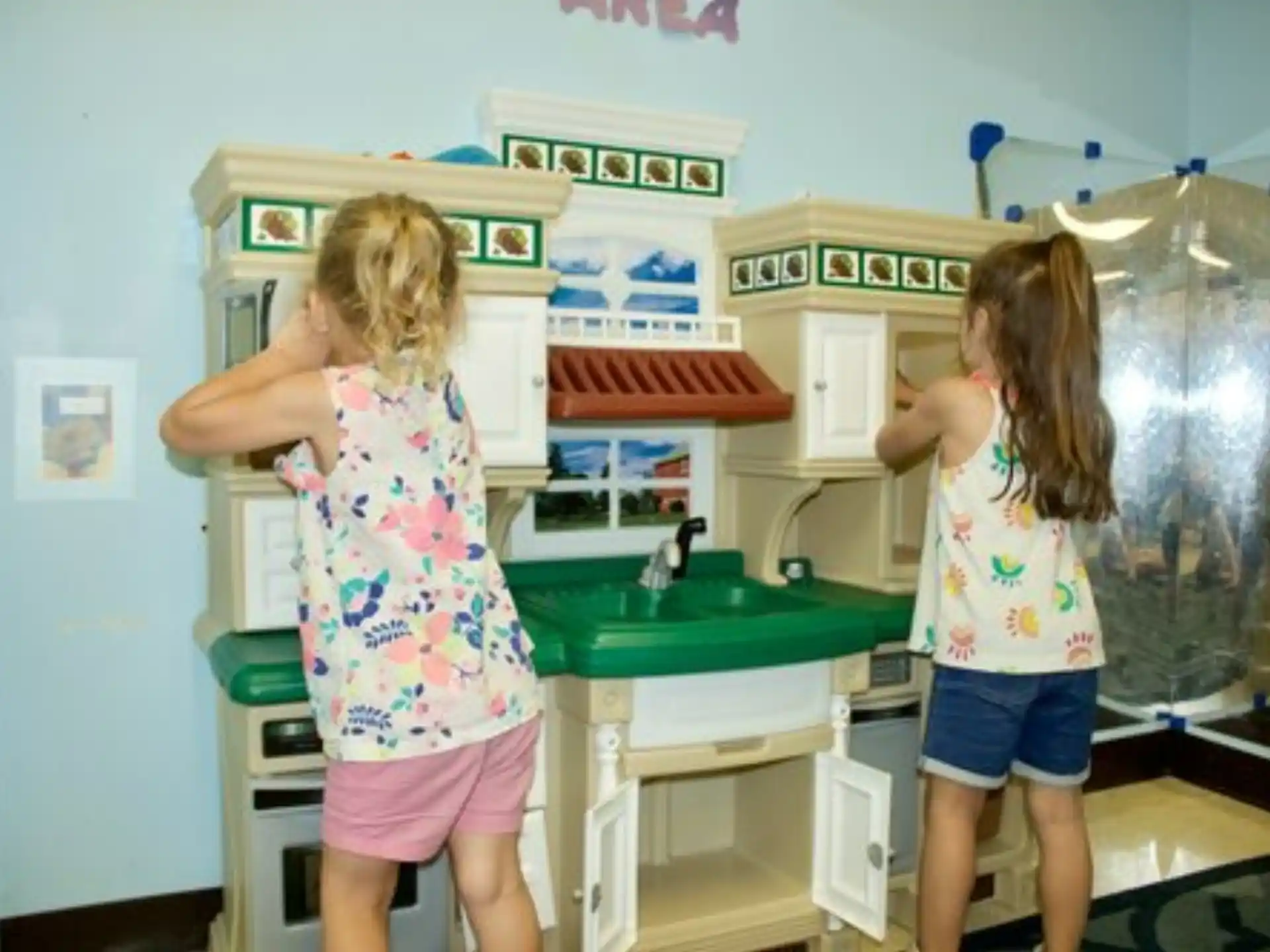 a couple of girls stand in a kitchen