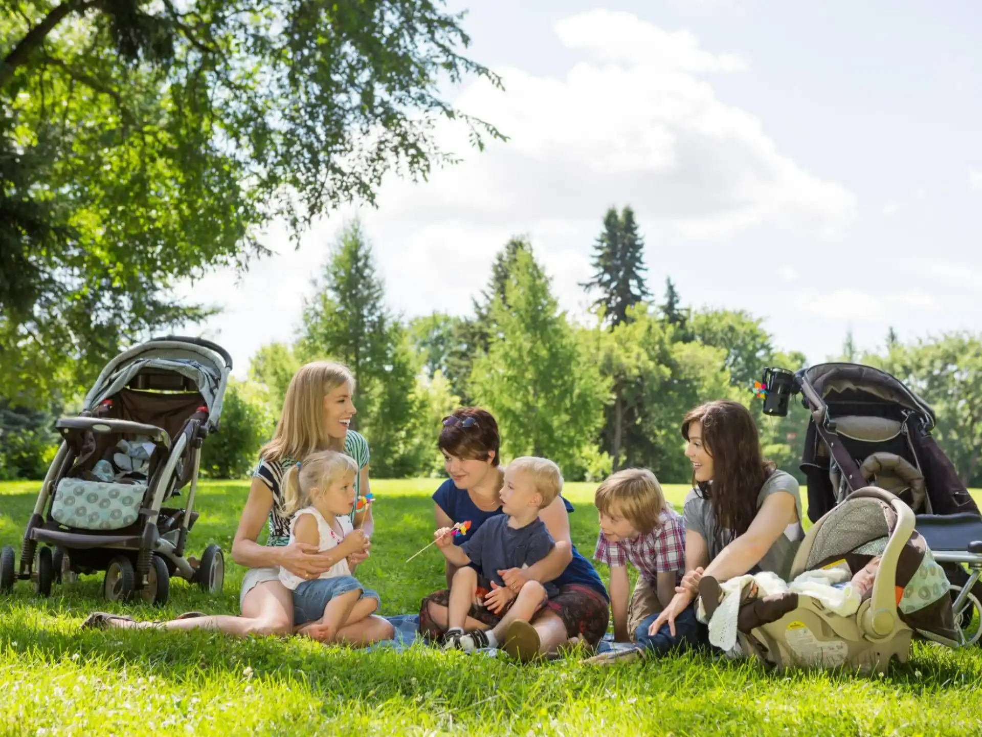 a group of people sitting on the grass with strollers and strollers