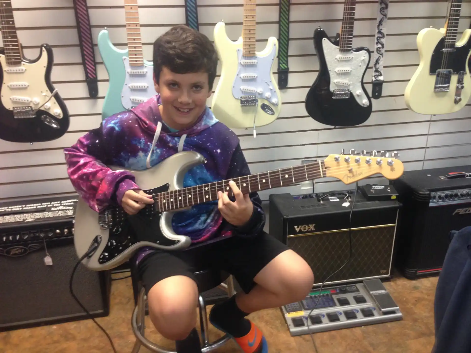 a boy sitting on a stool with a group of guitars