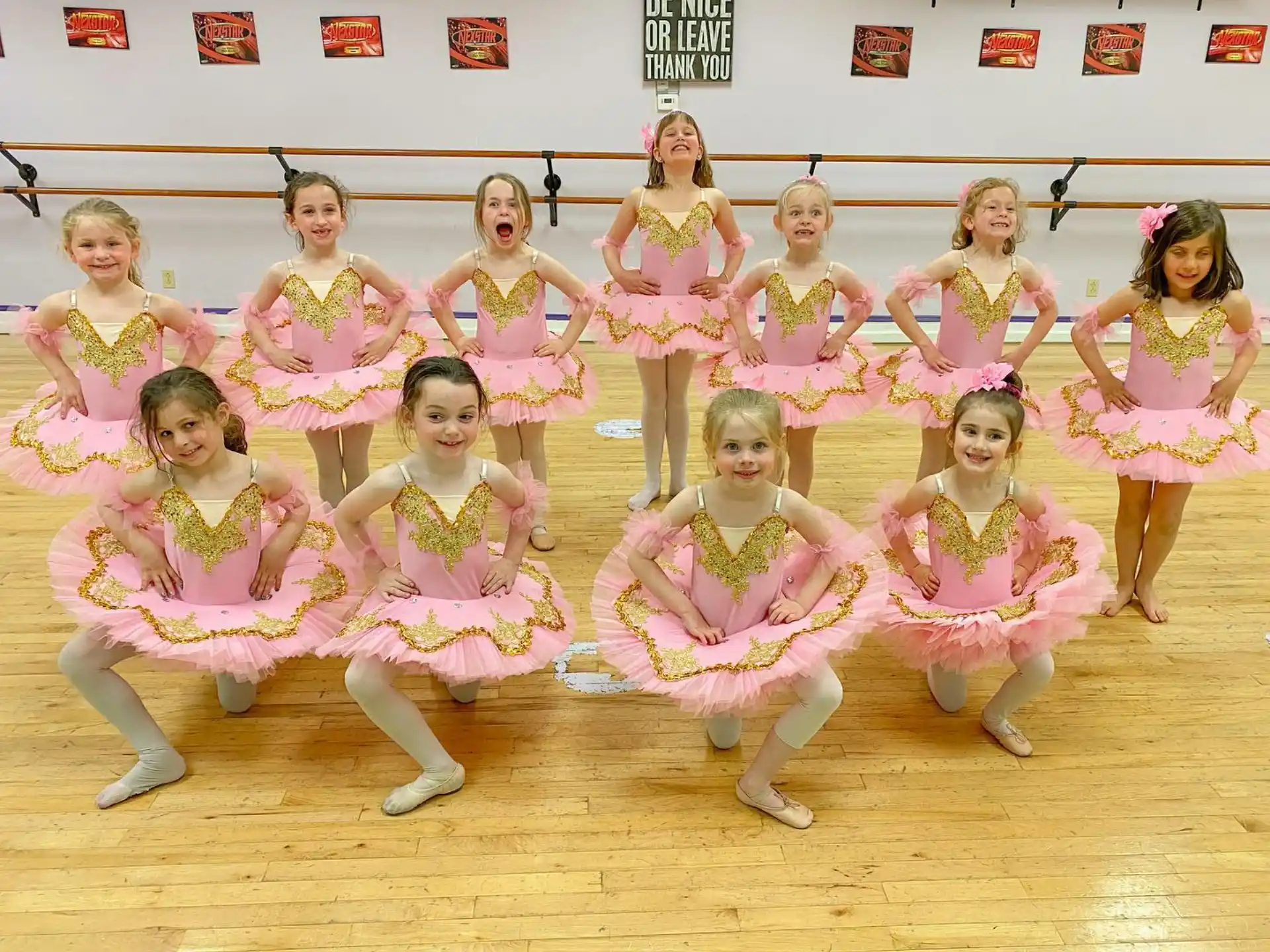 a group of girls wearing pink and white dresses on a wooden floor