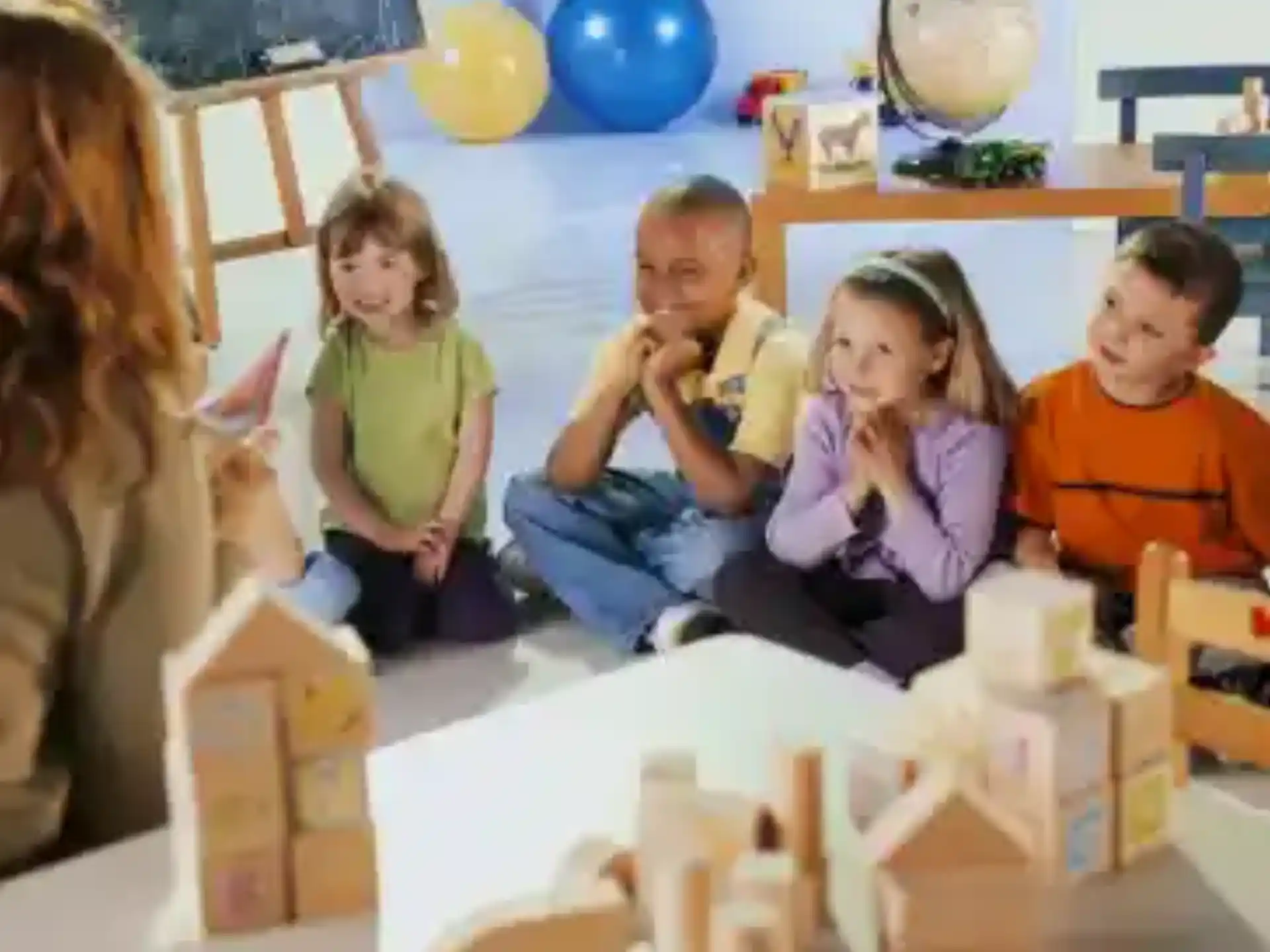 a group of children sitting on the floor with a table and a man and a woman standing in