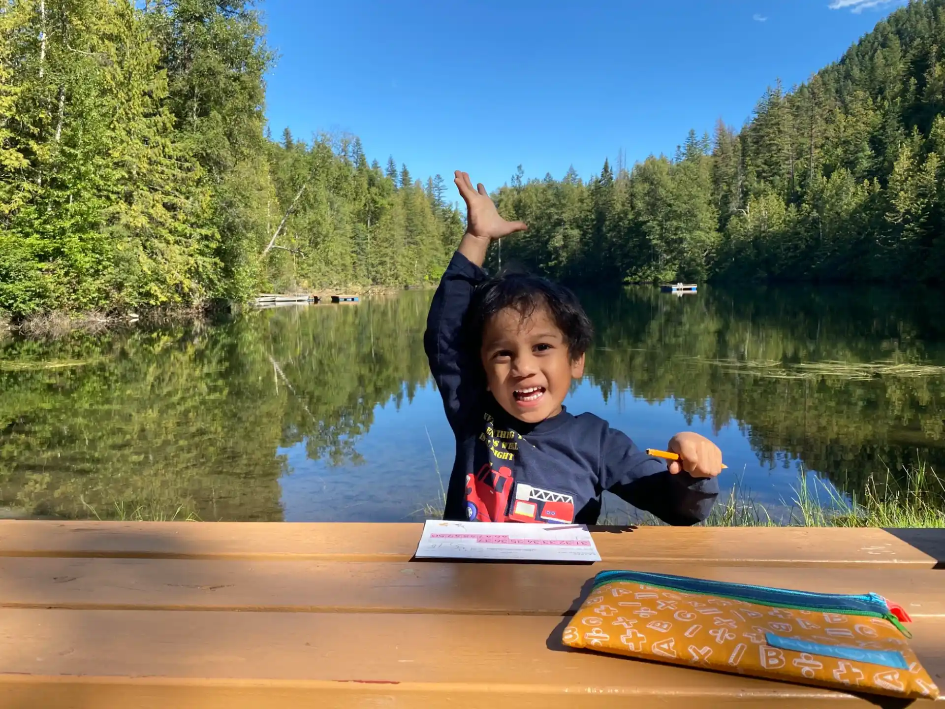a boy sitting on a dock by a lake with a book and a book
