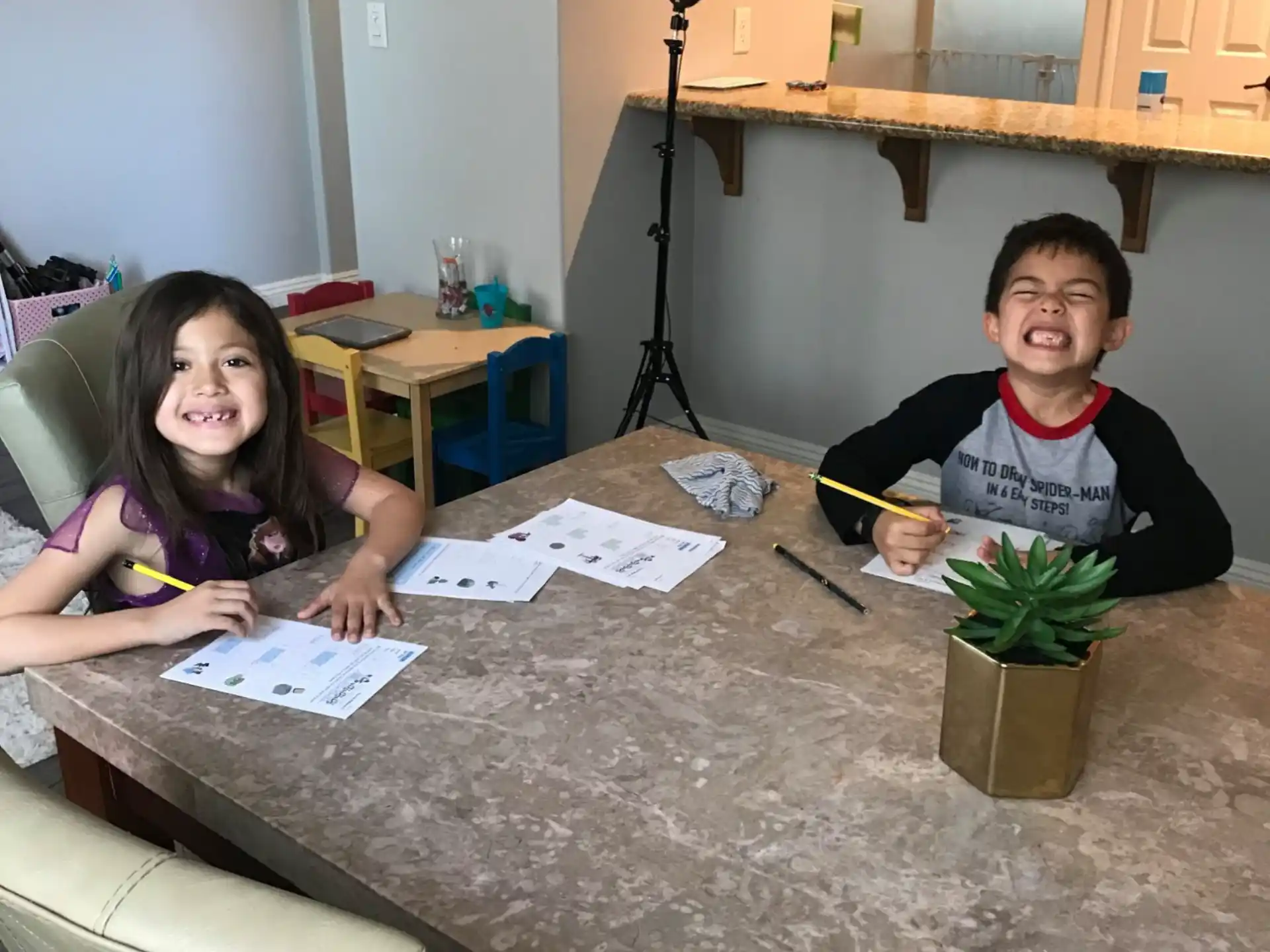 a boy and girl sitting at a table with papers and pens
