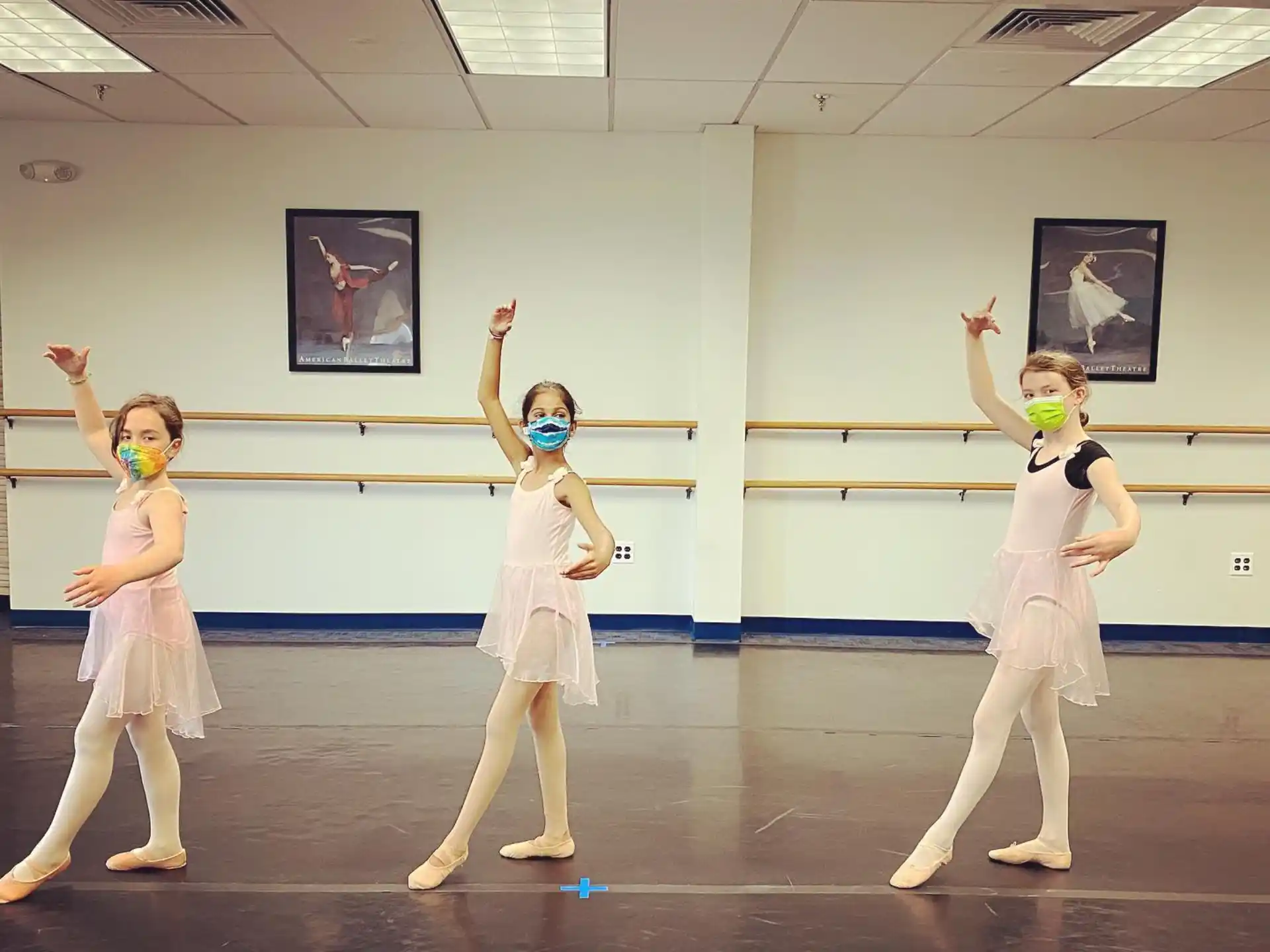 a group of girls in white outfits dancing in a room with pictures on the wall