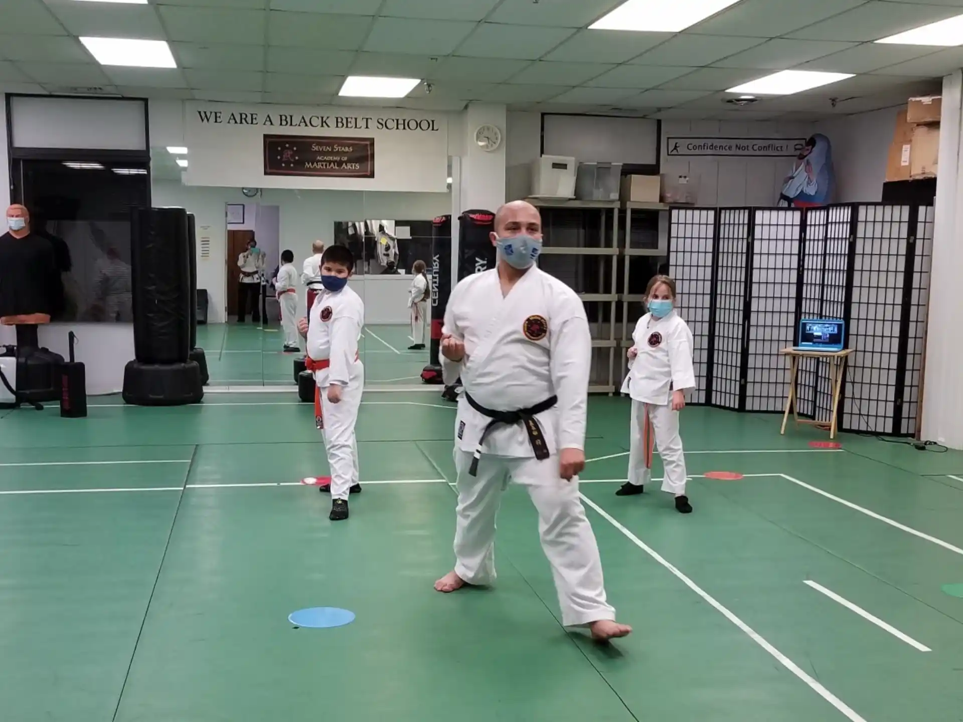 a group of people in white karate uniforms in a room with a green floor and a green mat