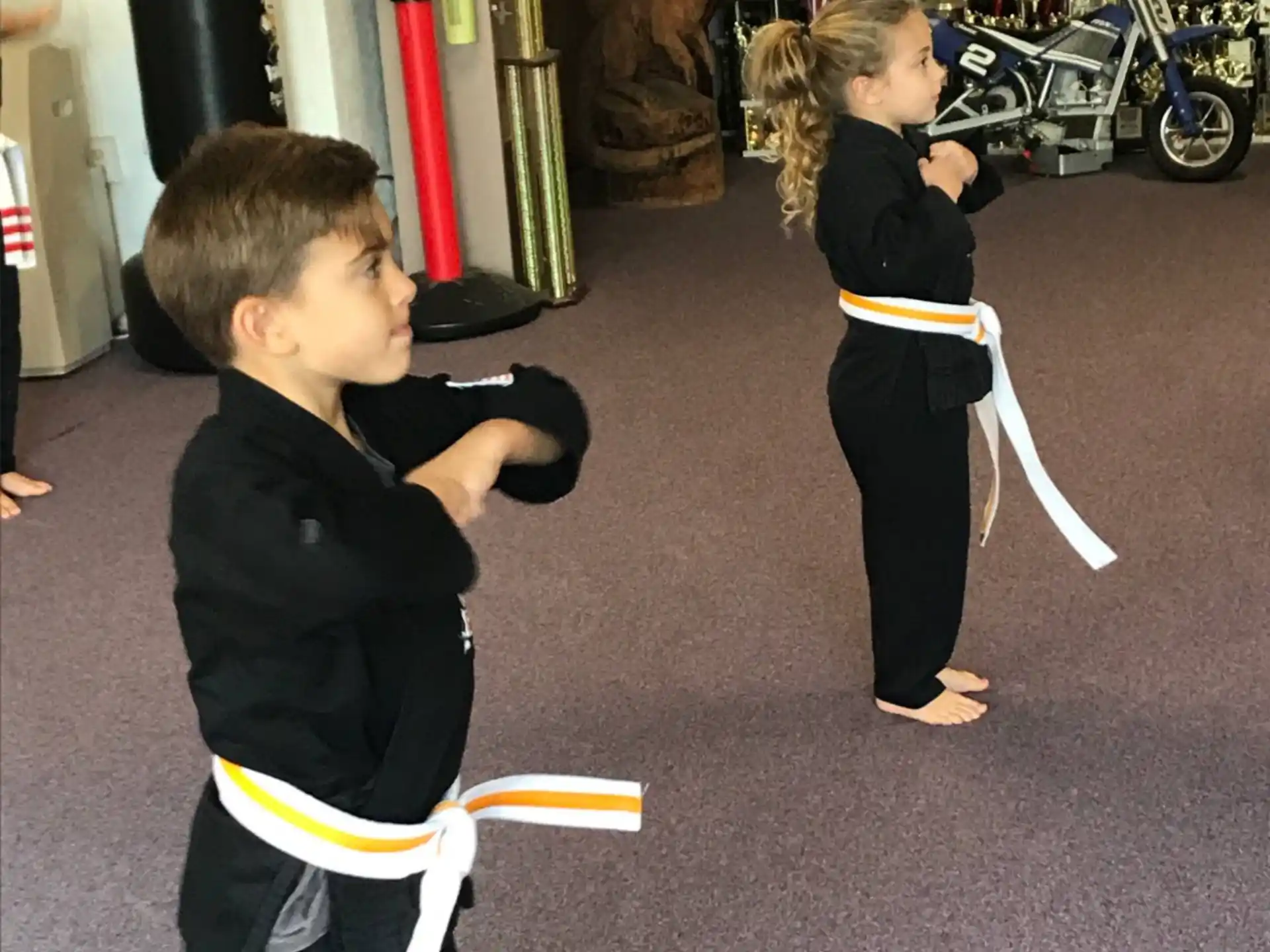 a couple of children in black karate uniforms in a room with a motorcycle and a bike and a