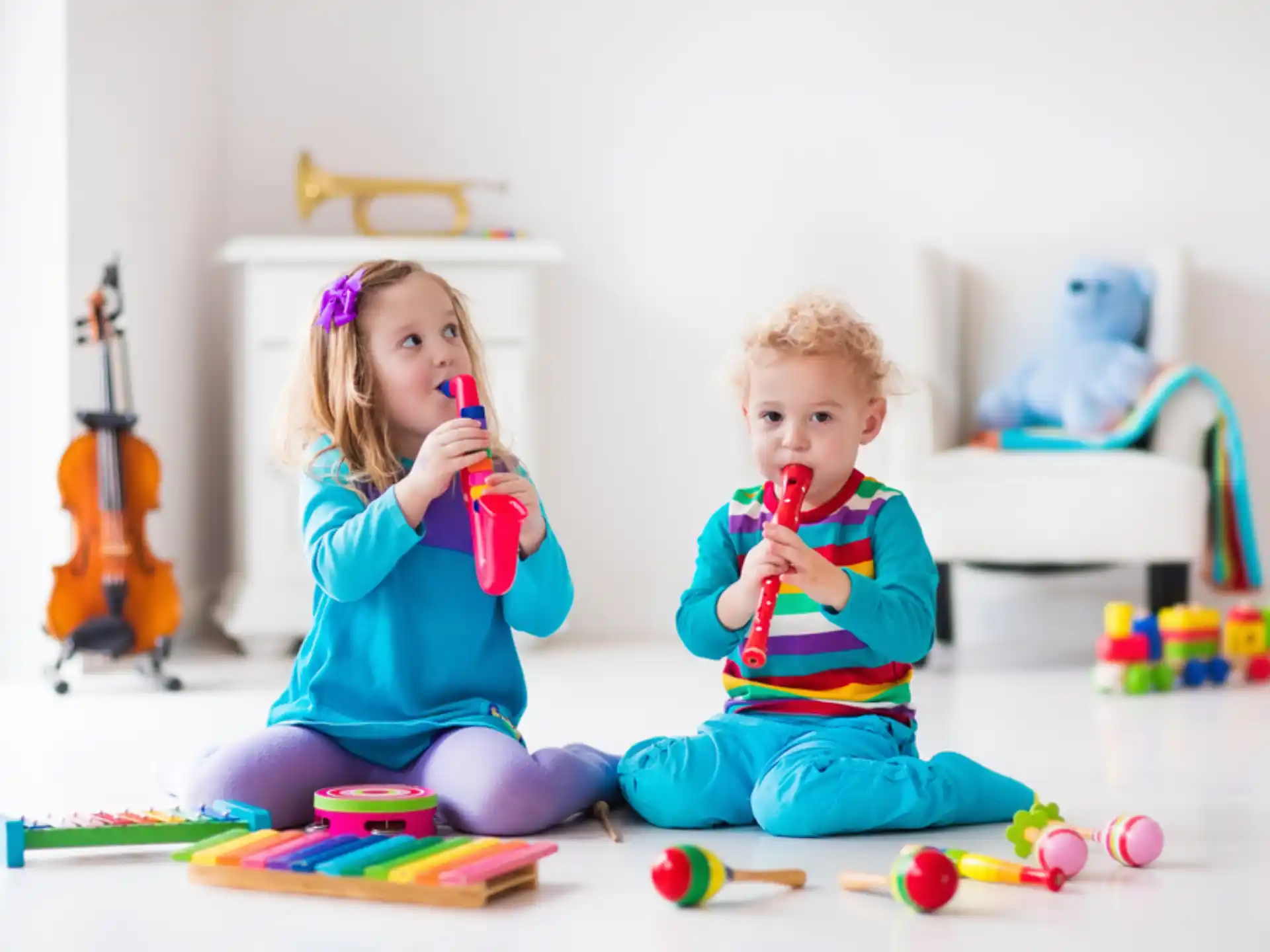 a couple of kids sitting on the floor with toys and a guitar