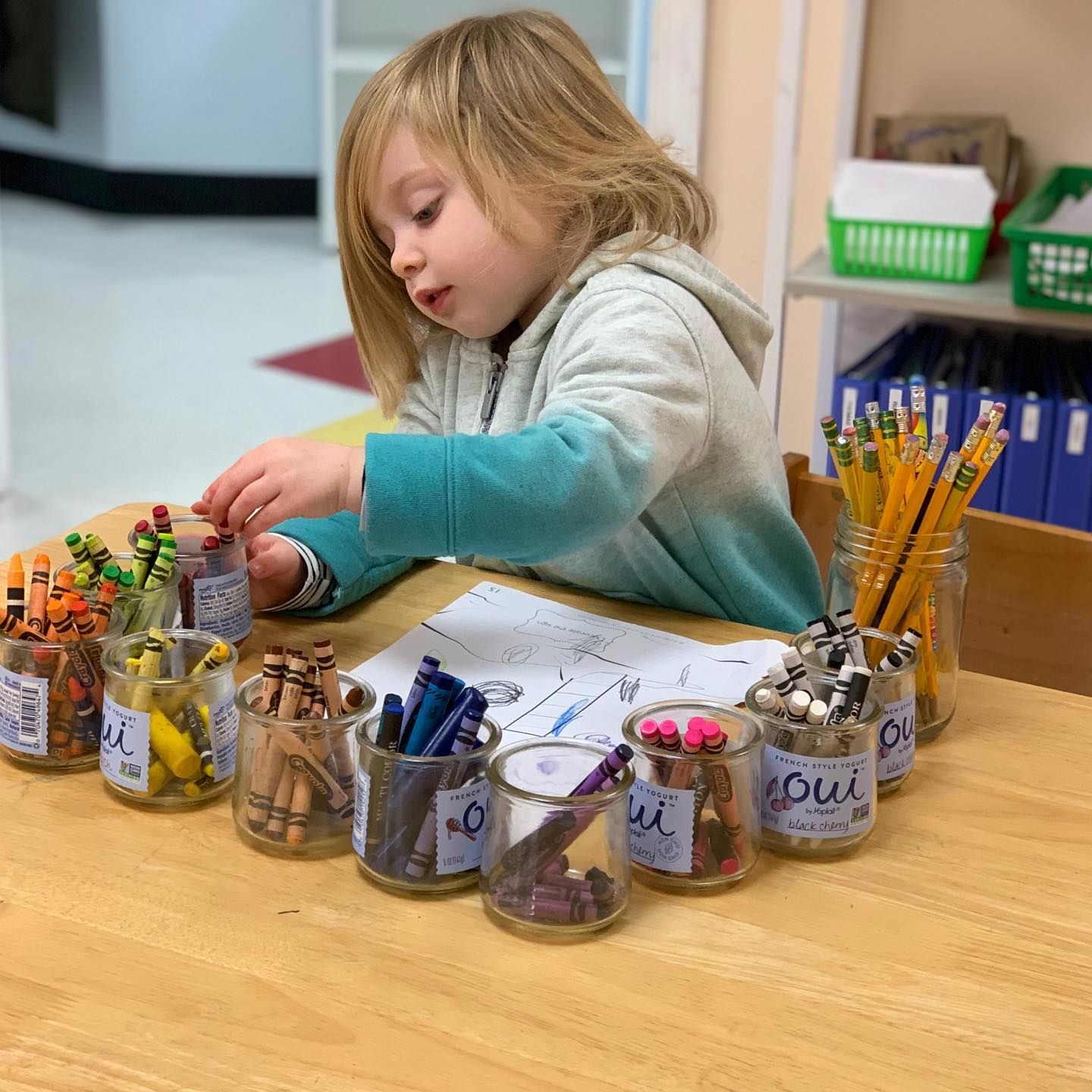 a girl sitting at a table with many jars of jams