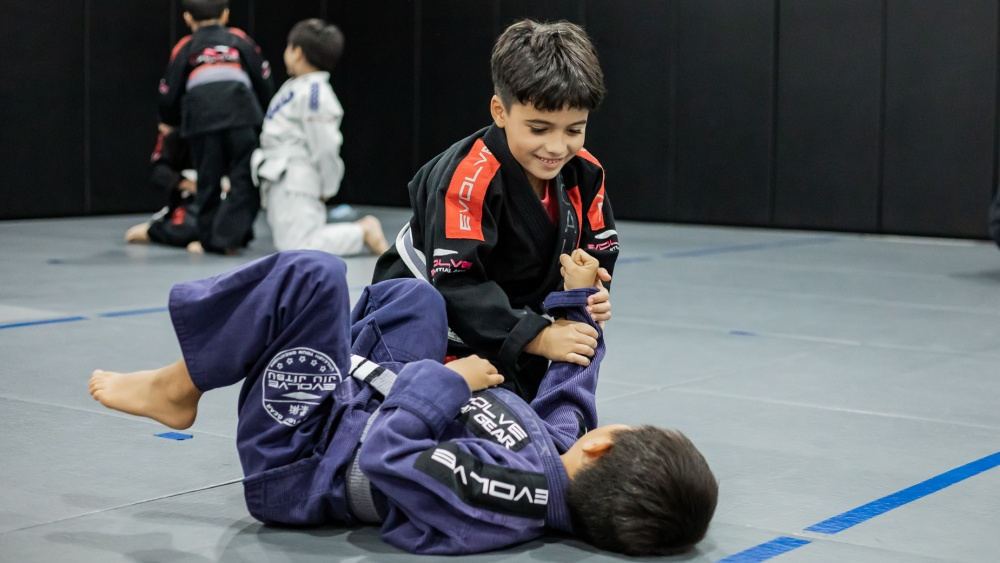 a boy in a uniform kneeling on the ground with another boy in the back