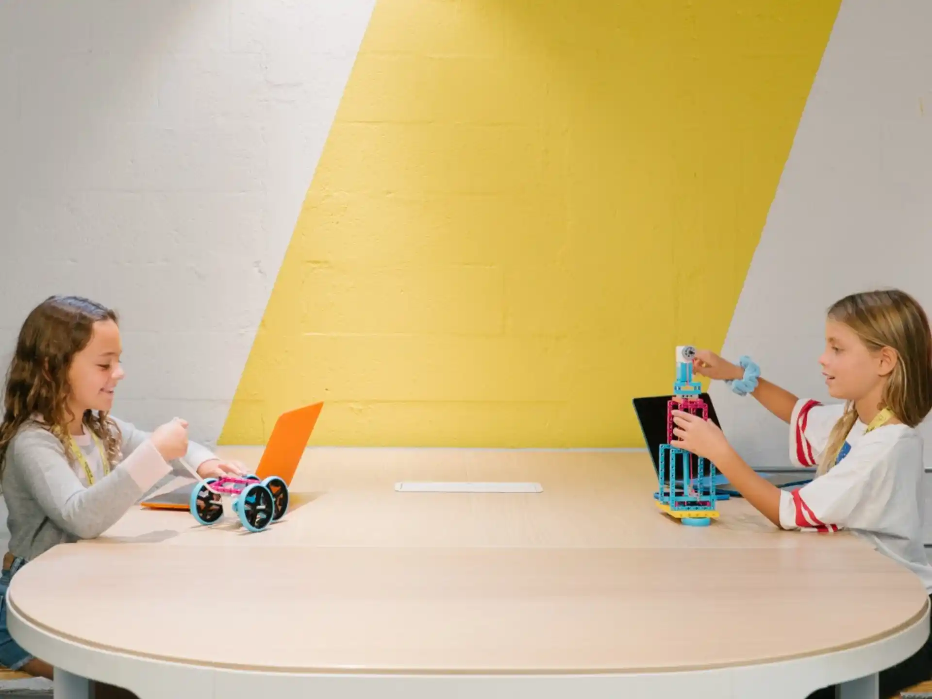 a couple of girls sitting at a table with a toy
