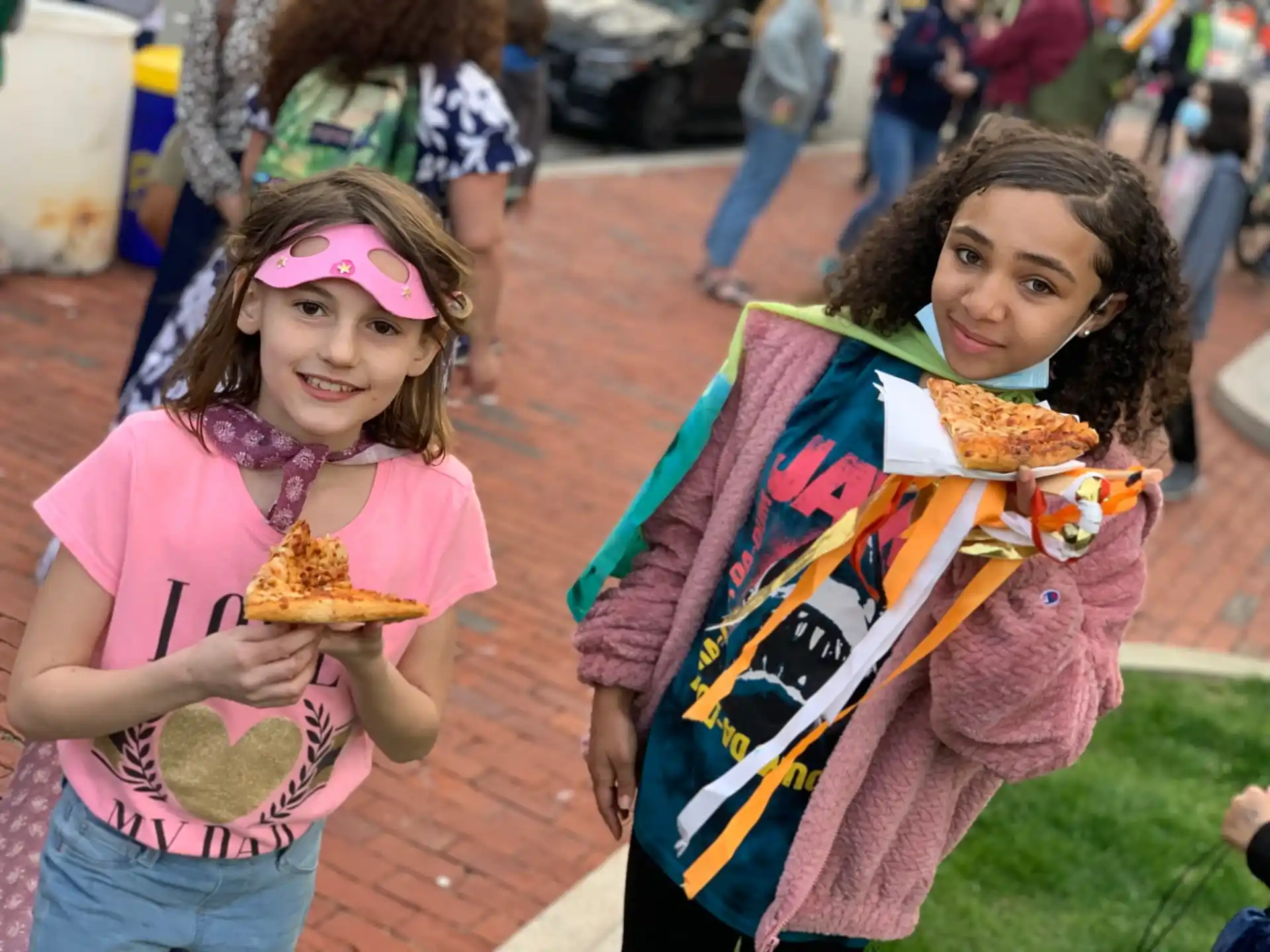 girls eating pizzas on the sidewalk