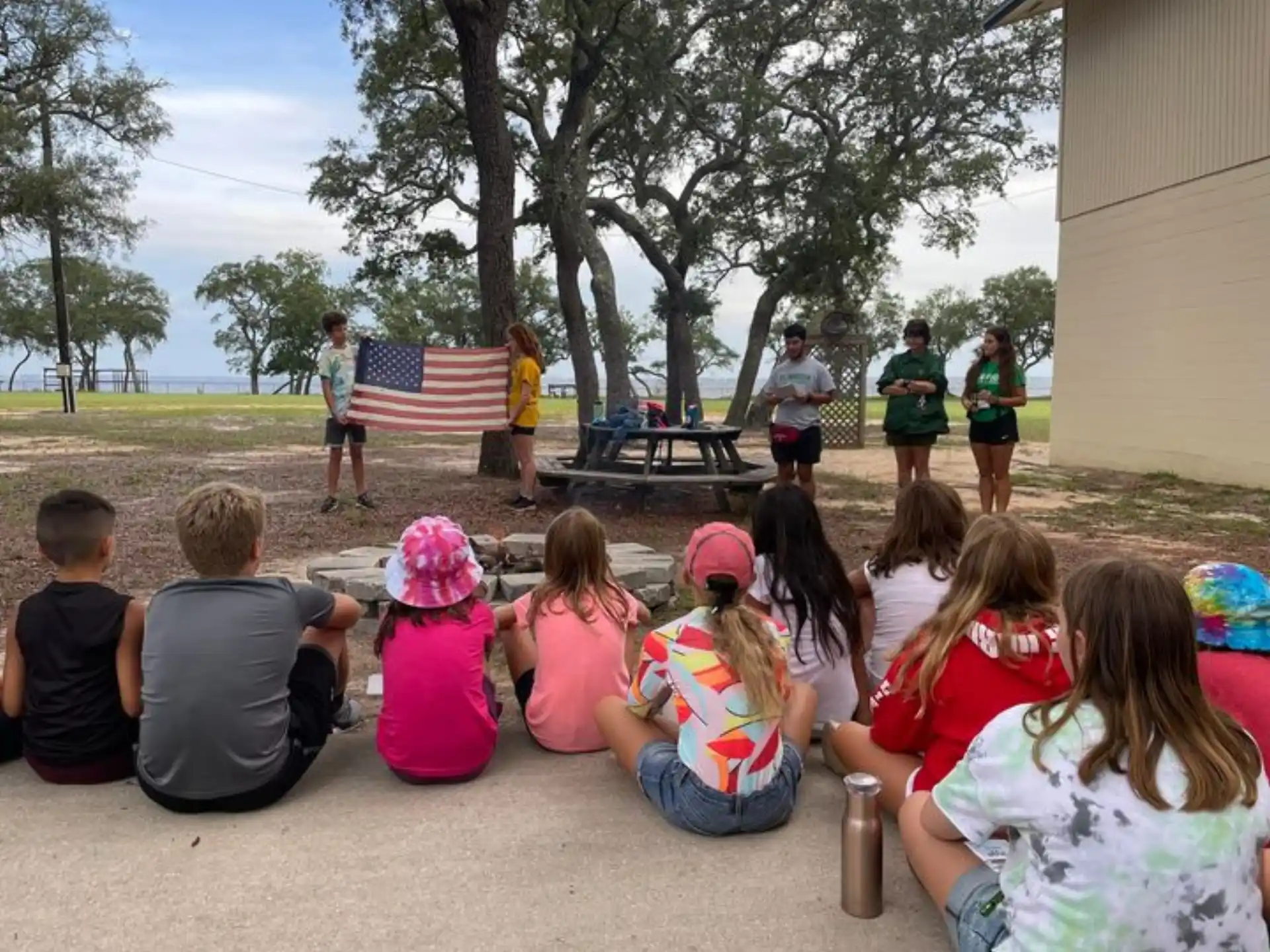 a group of children sitting on the ground in front of a flag