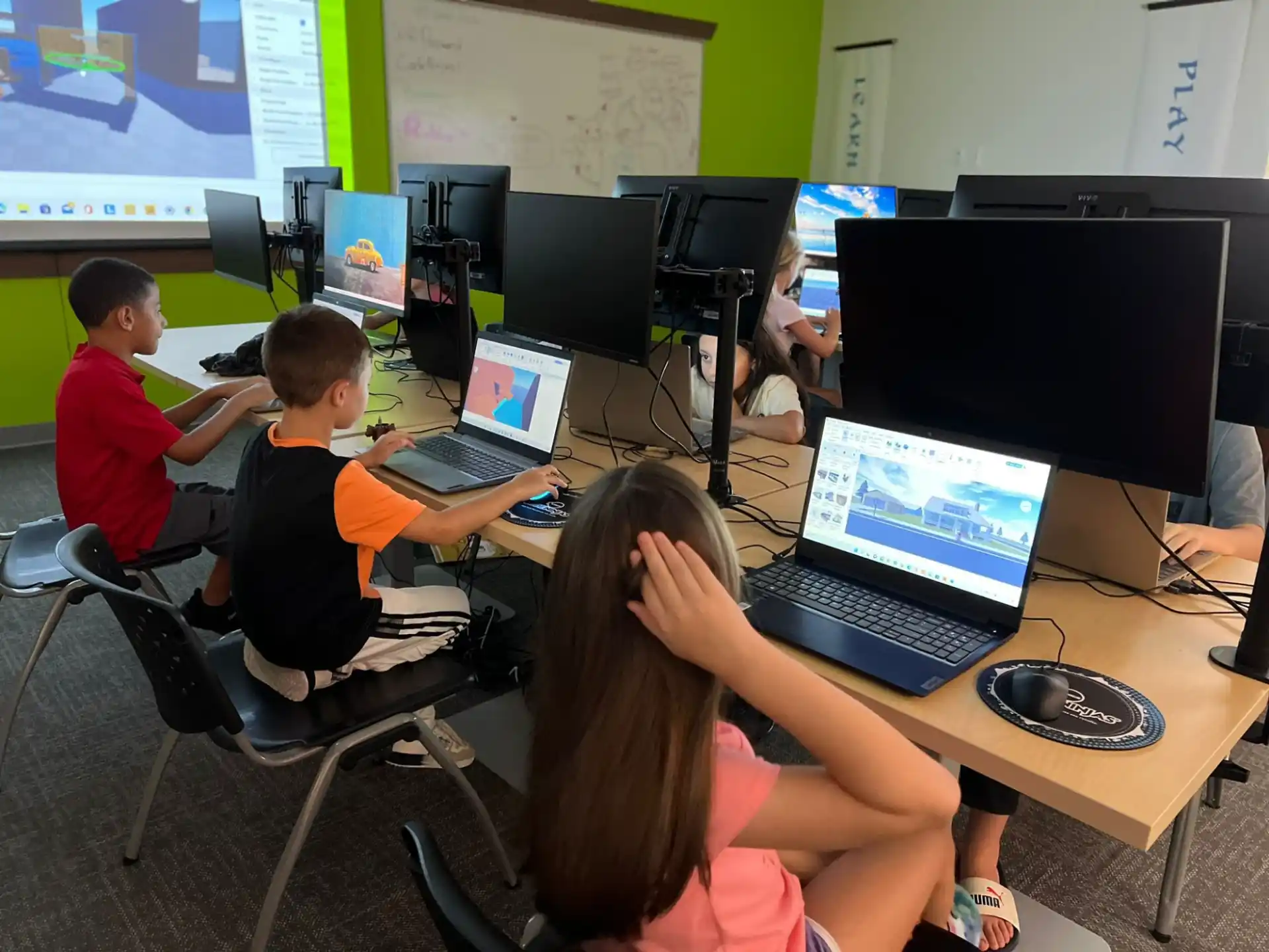 a group of kids sitting at a table with laptops
