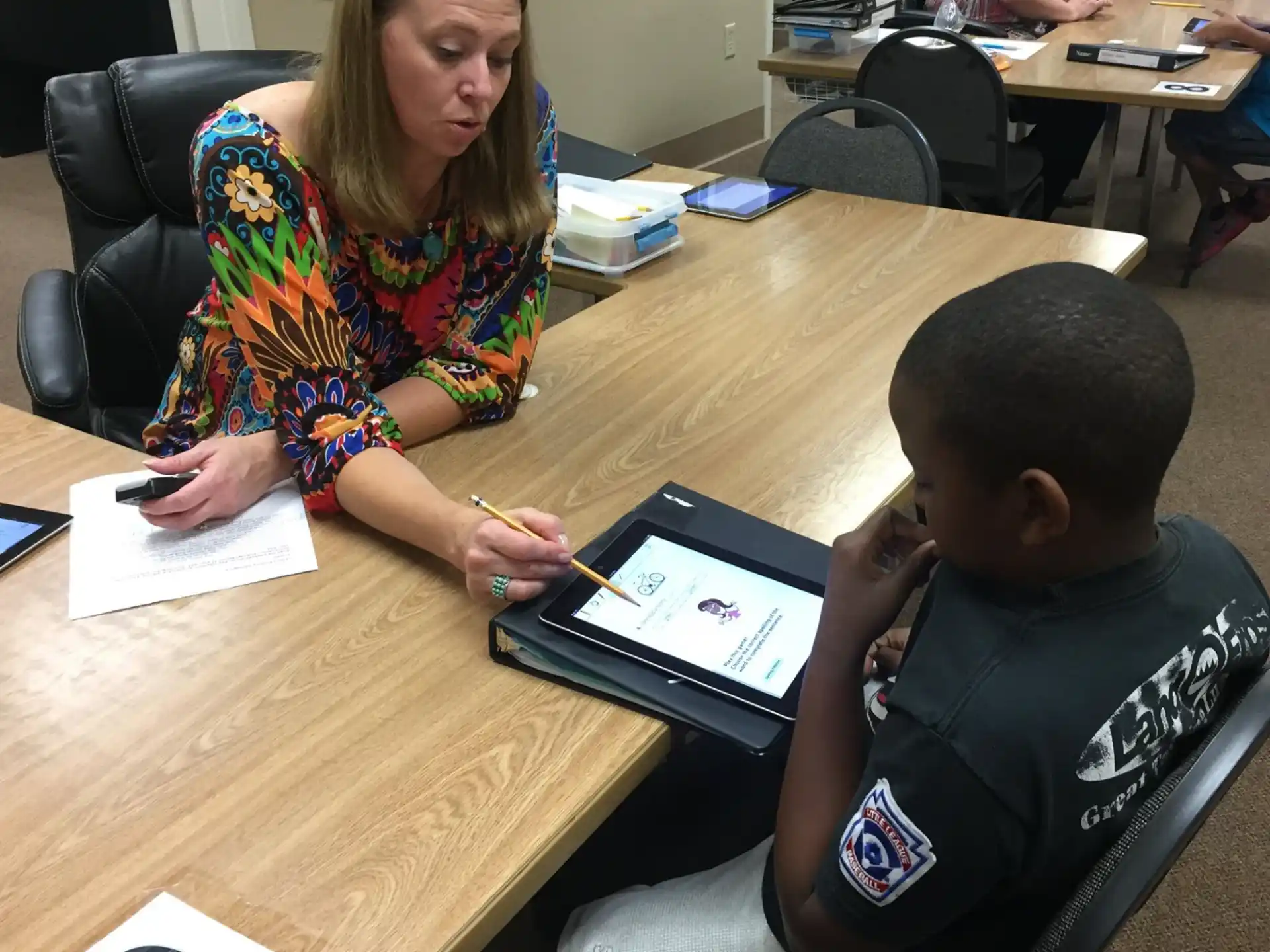 a person and a boy sitting at a table looking at a tablet