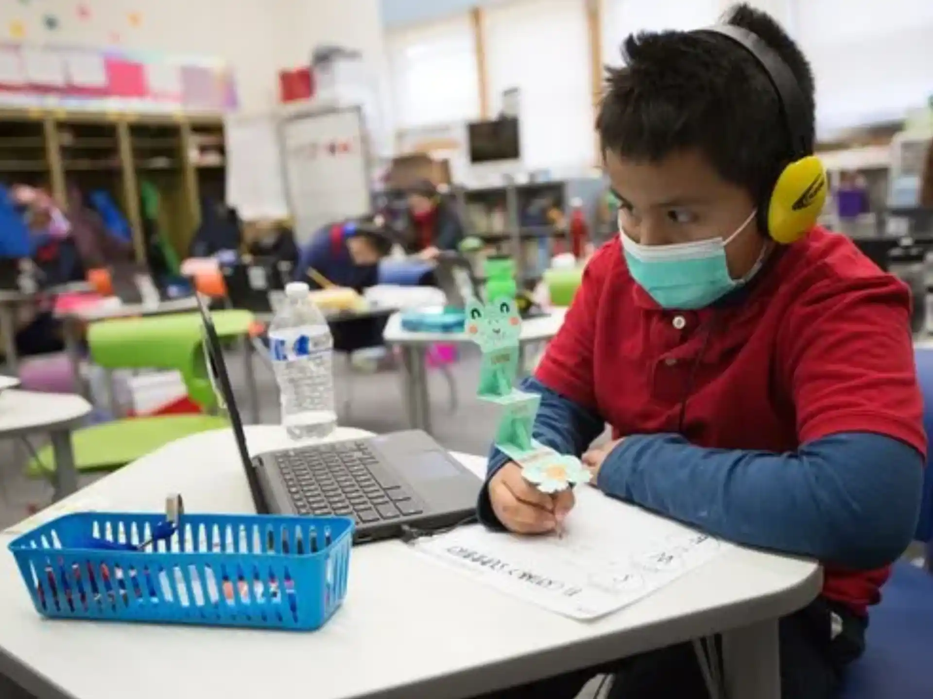 a young boy wearing a mask and working on a laptop