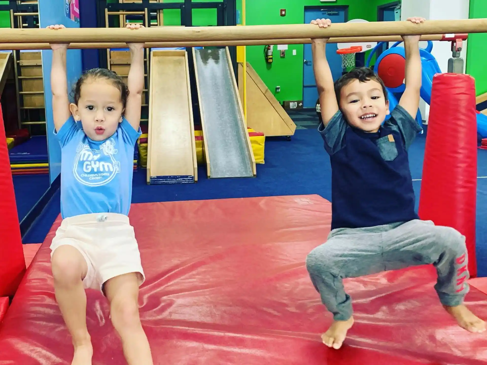 a couple of kids playing on a red mat in a gym