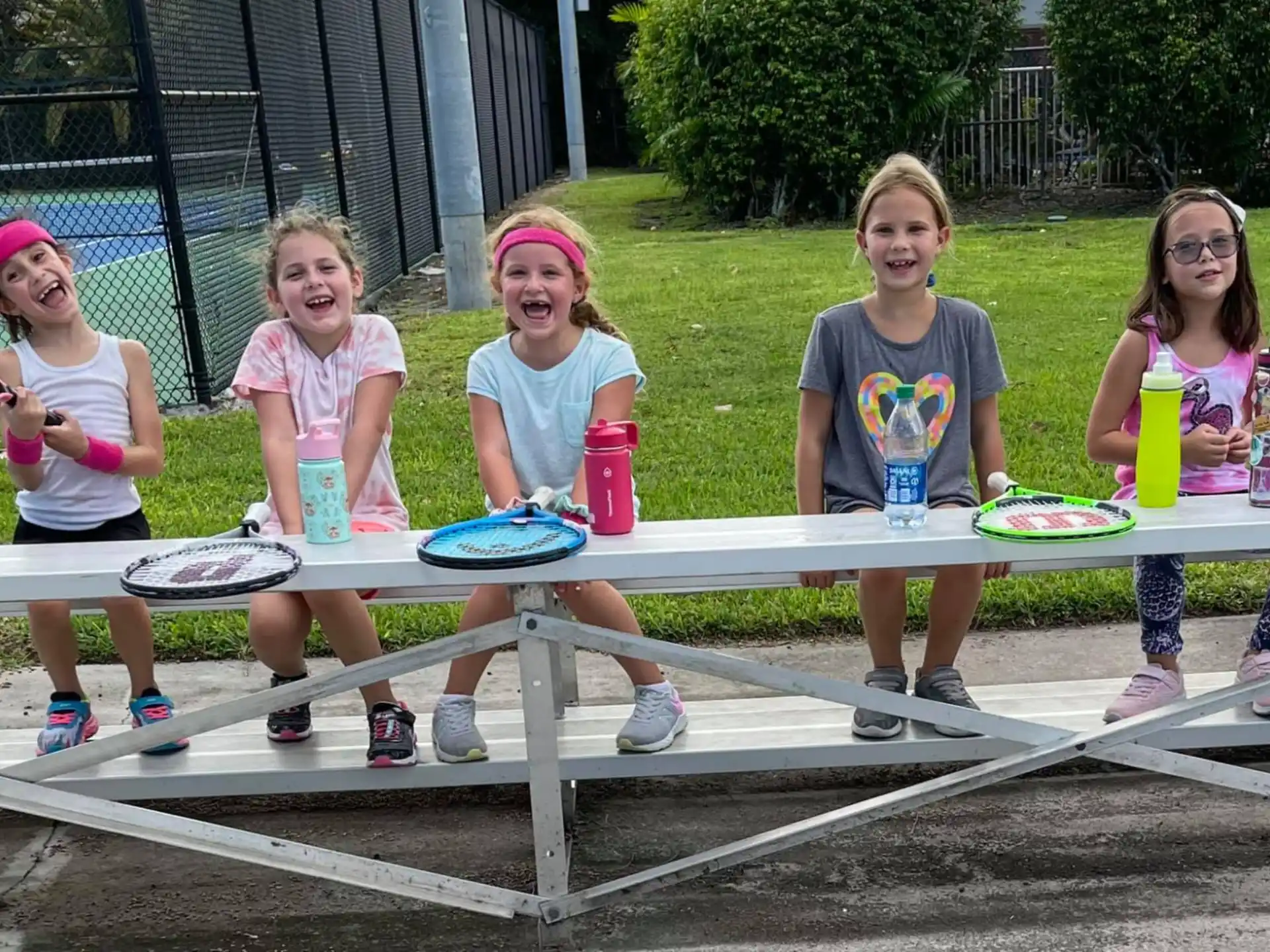 a group of kids sitting on a bench with a racket and cups