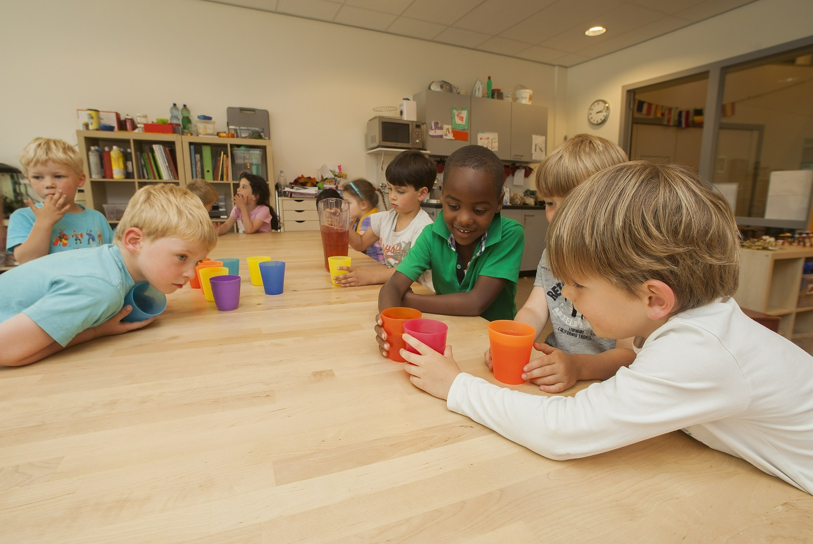 a group of children sitting at a table with cups and a book