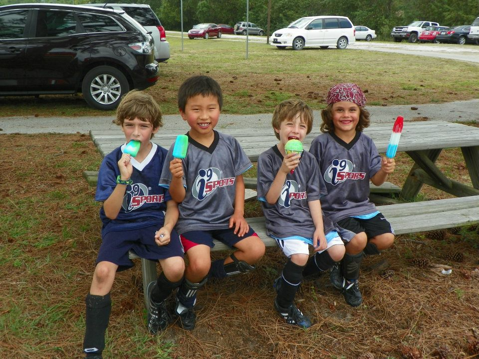 a group of kids sitting on a bench with green cups in their hands